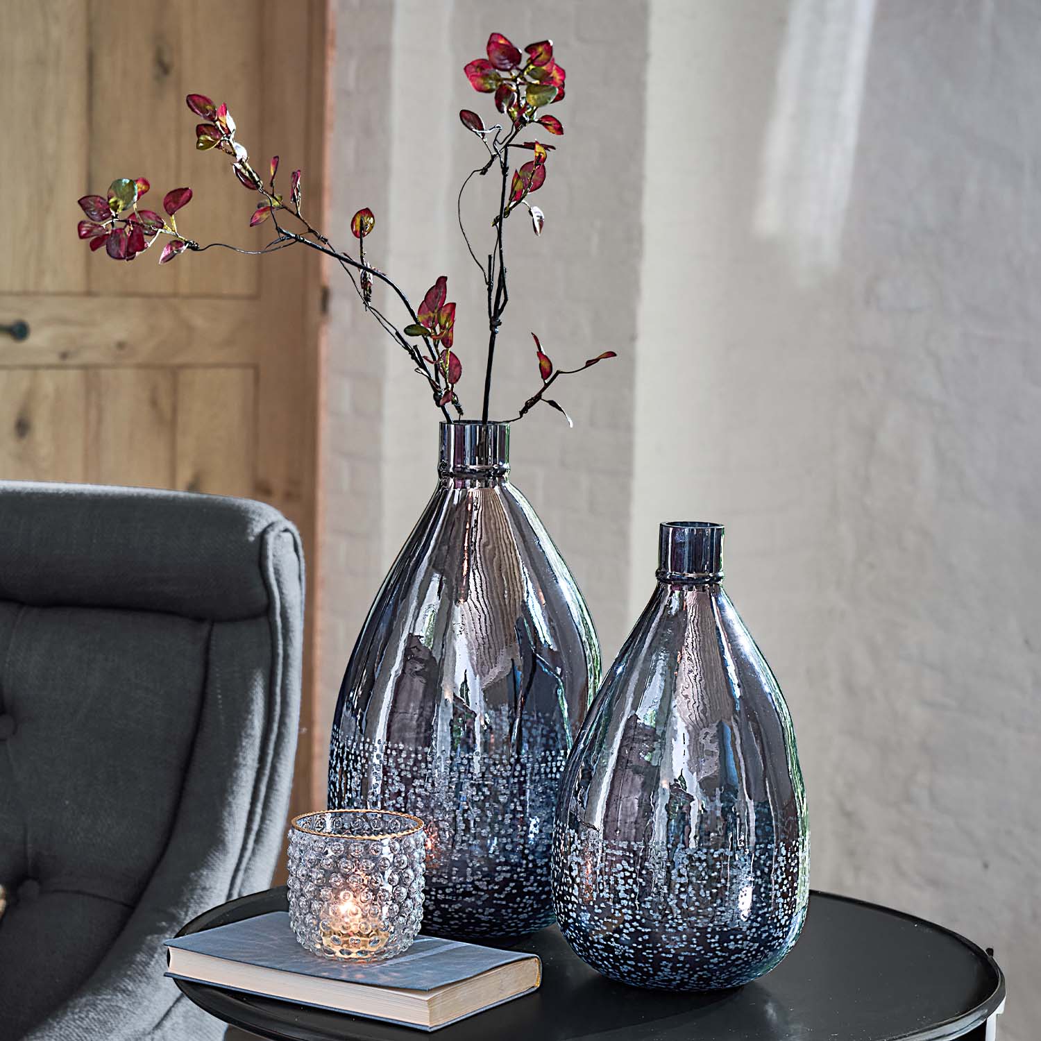 Deux vases décoratifs en verre fumé avec motif à bulles sur une table noire à côté d'un photophore et d'un livre