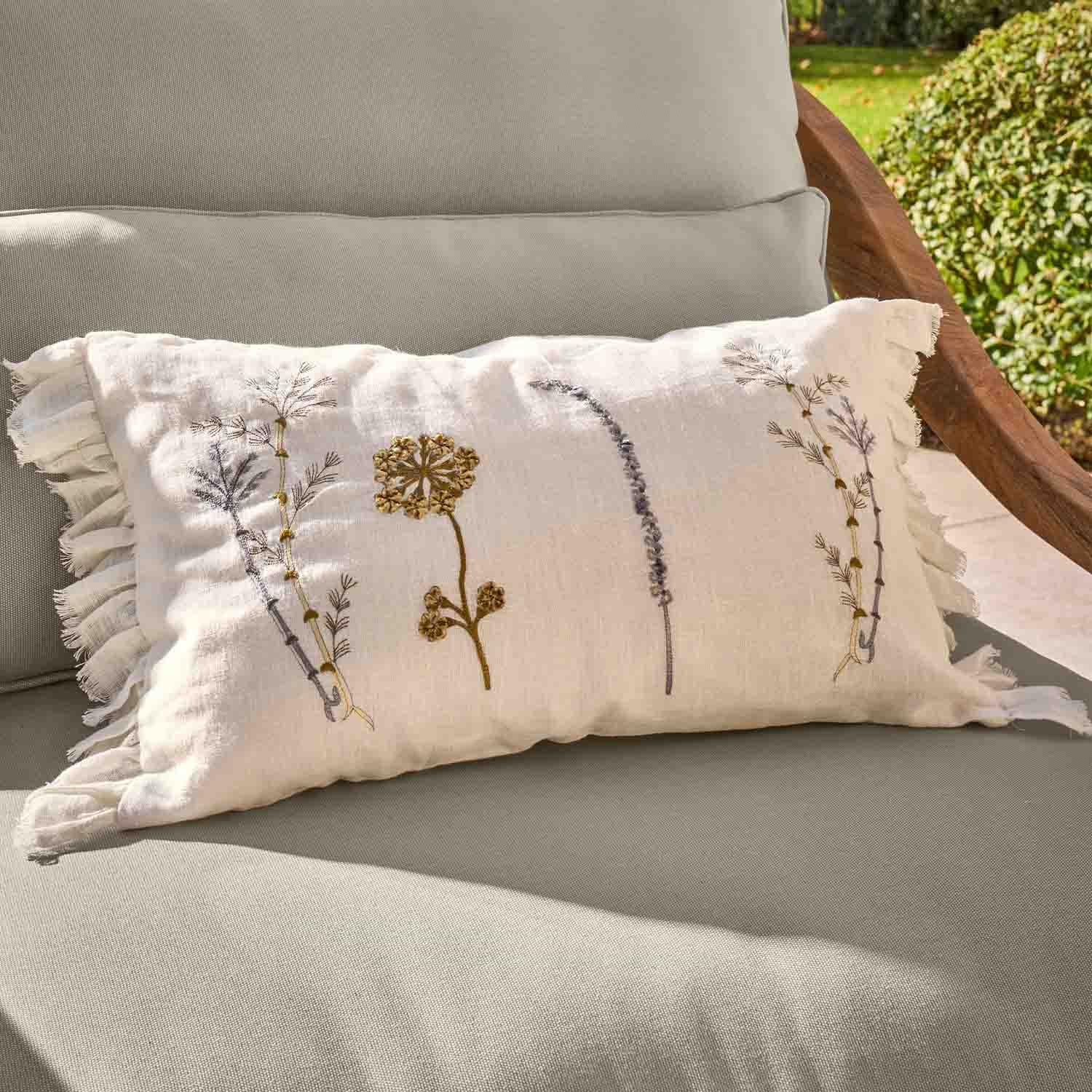 Coussin rectangulaire en lin blanc avec broderie florale et volant sur fauteuil gris extérieur