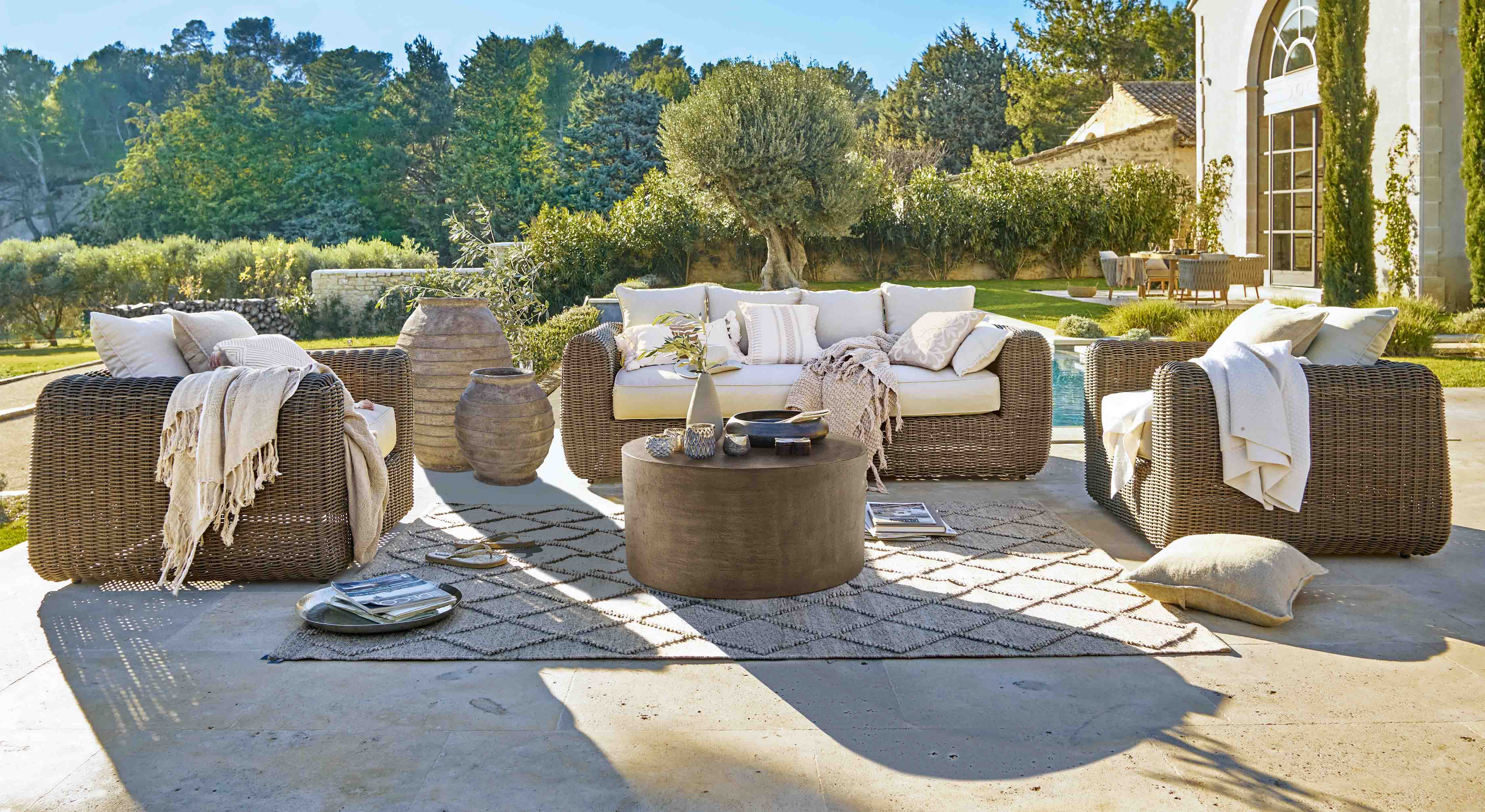Ensemble de mobilier de jardin en rotin brun avec coussins crème et table basse sur terrasse ensoleillée
