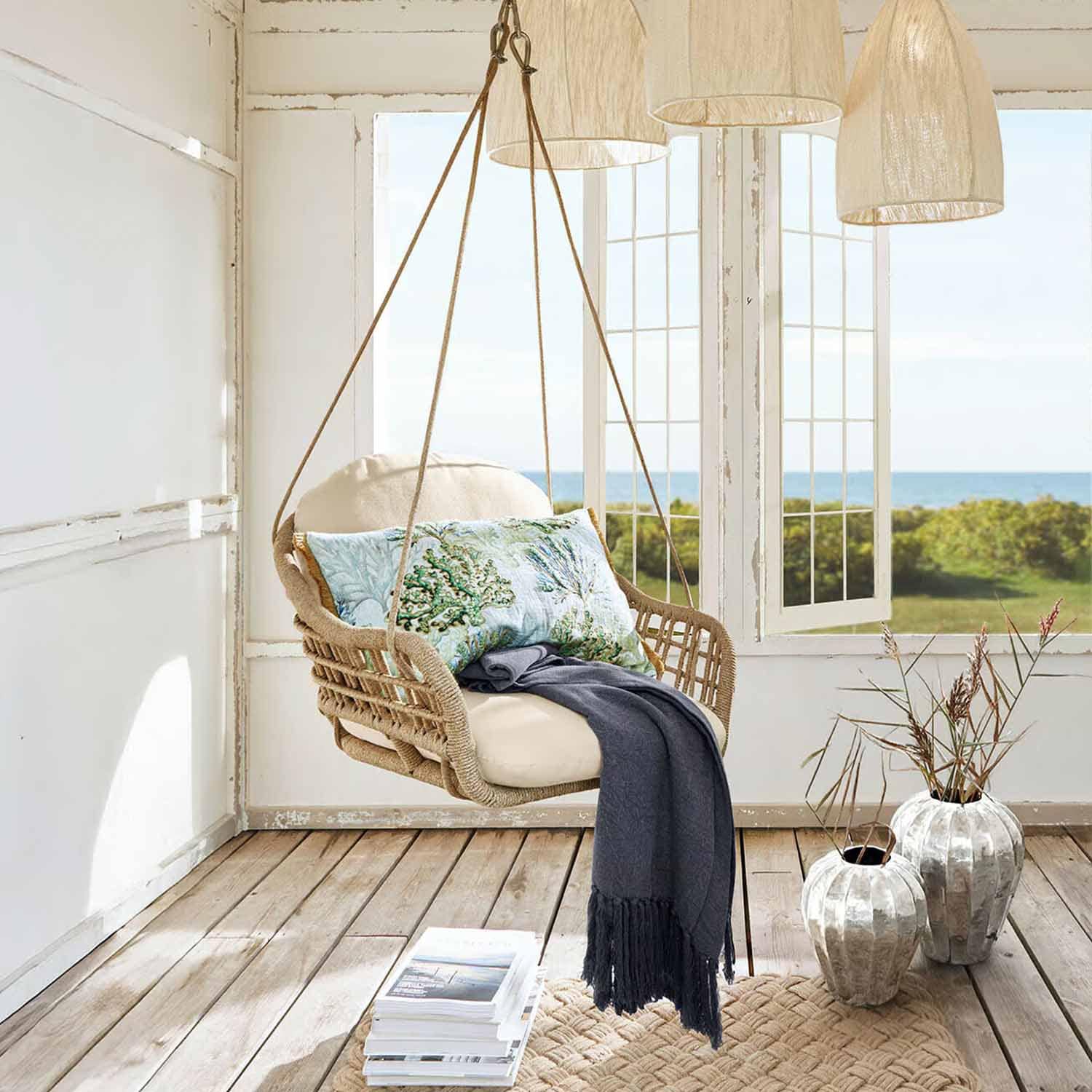 Fauteuil suspendu en corde tressée beige avec coussin crème et plaid bleu foncé dans une pièce lumineuse