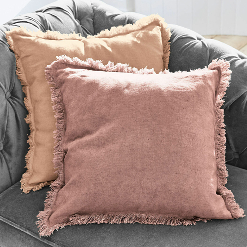 Deux coussins décoratifs en lin rose et beige avec franges sur un canapé gris, ambiance cosy