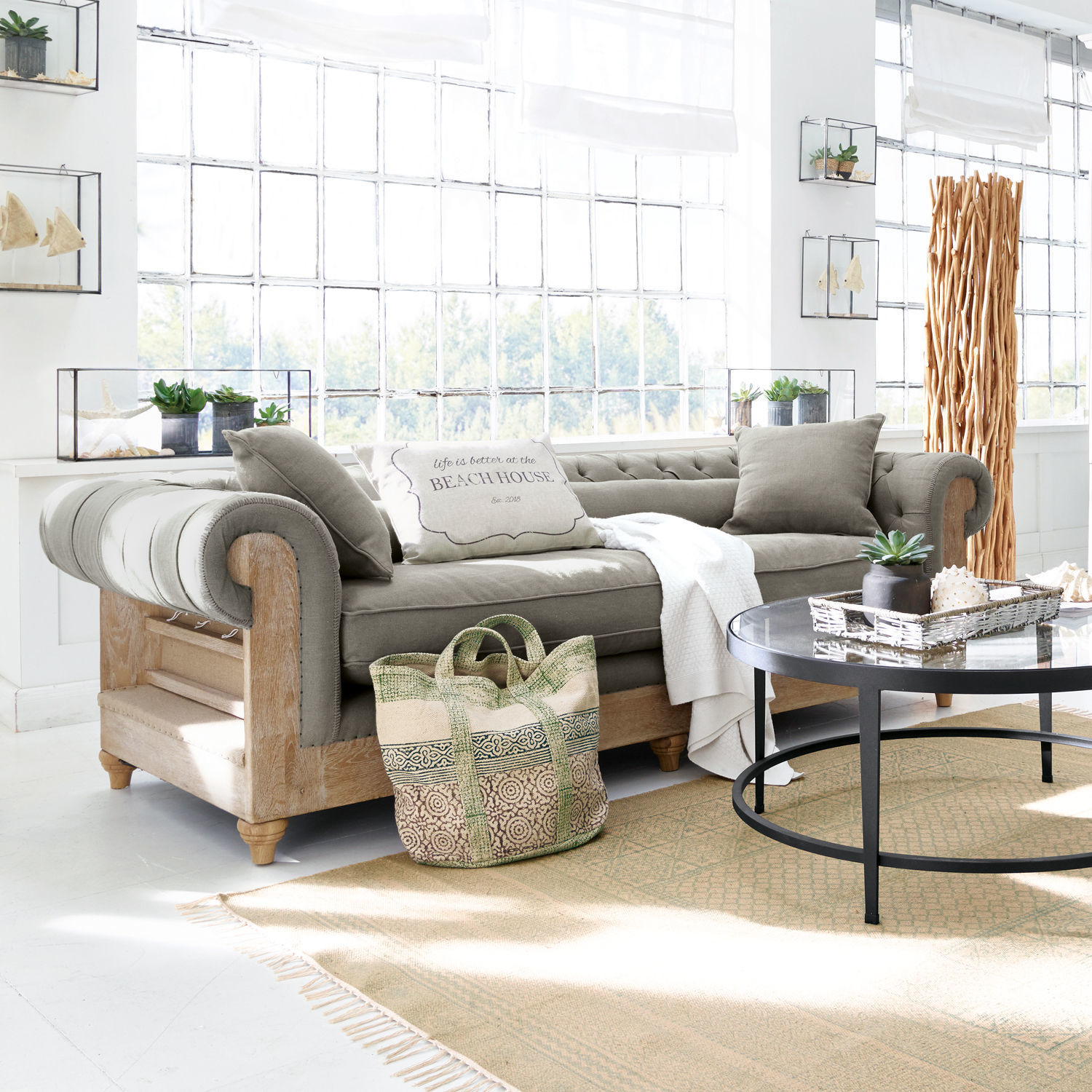 Canapé Kanani Canapé gris avec cadre en bois dans un salon lumineux décoré avec table basse ronde et plantes