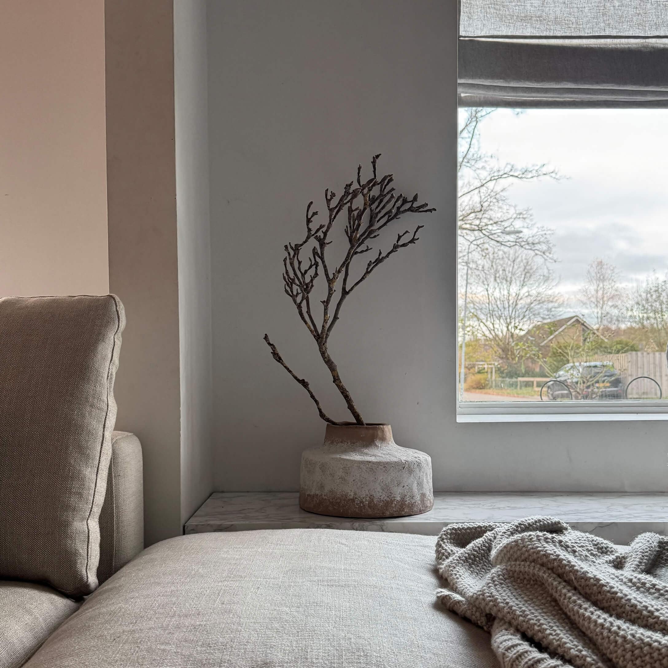 Vase en céramique beige avec branche sèche sur le rebord de fenêtre dans un salon lumineux