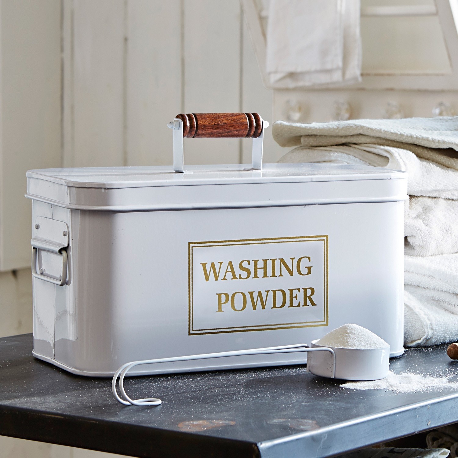 Boîte à lessive Washing Boîte métallique blanche pour poudre à laver avec poignée en bois et mesurette sur table noire
