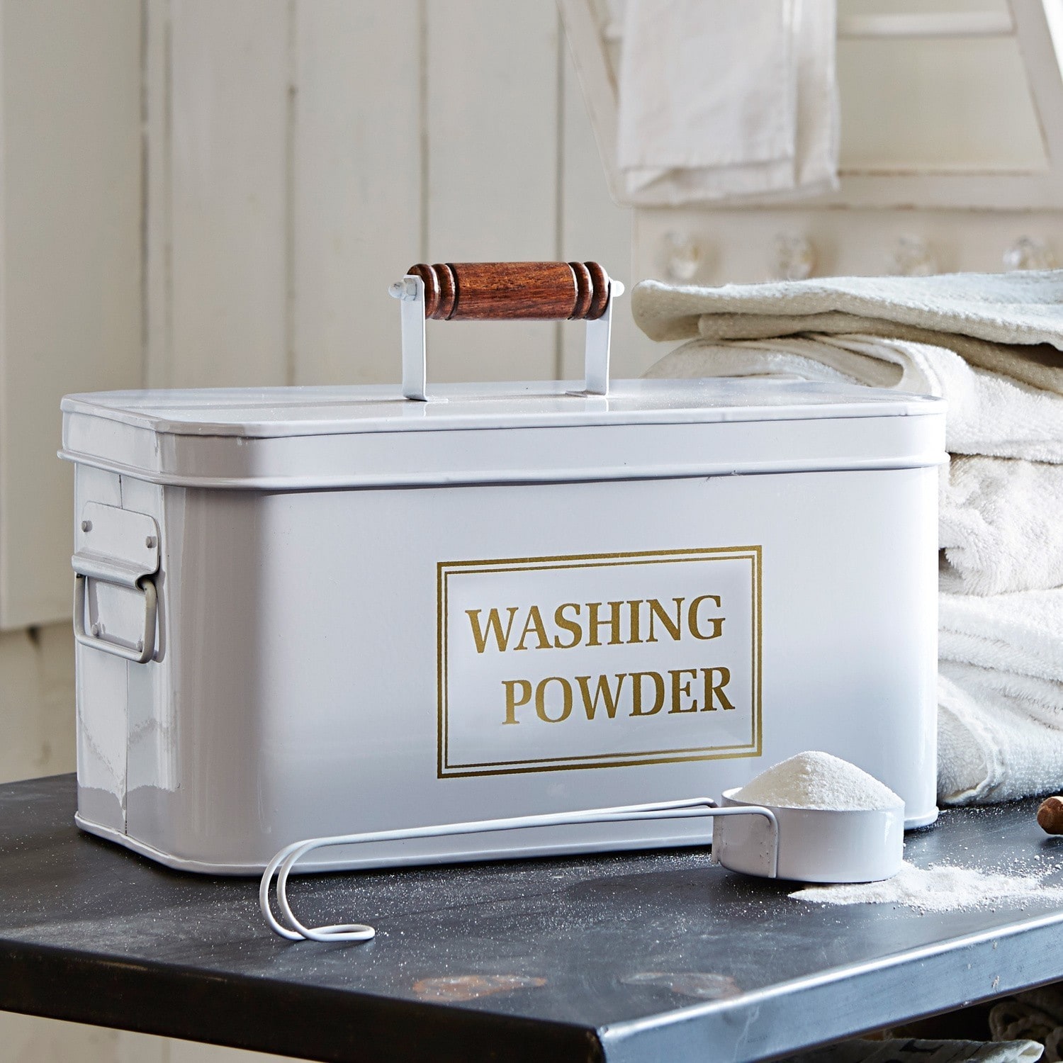 Boîte à lessive Washing Boîte métallique blanche pour poudre à laver avec poignée en bois et mesurette sur table noire