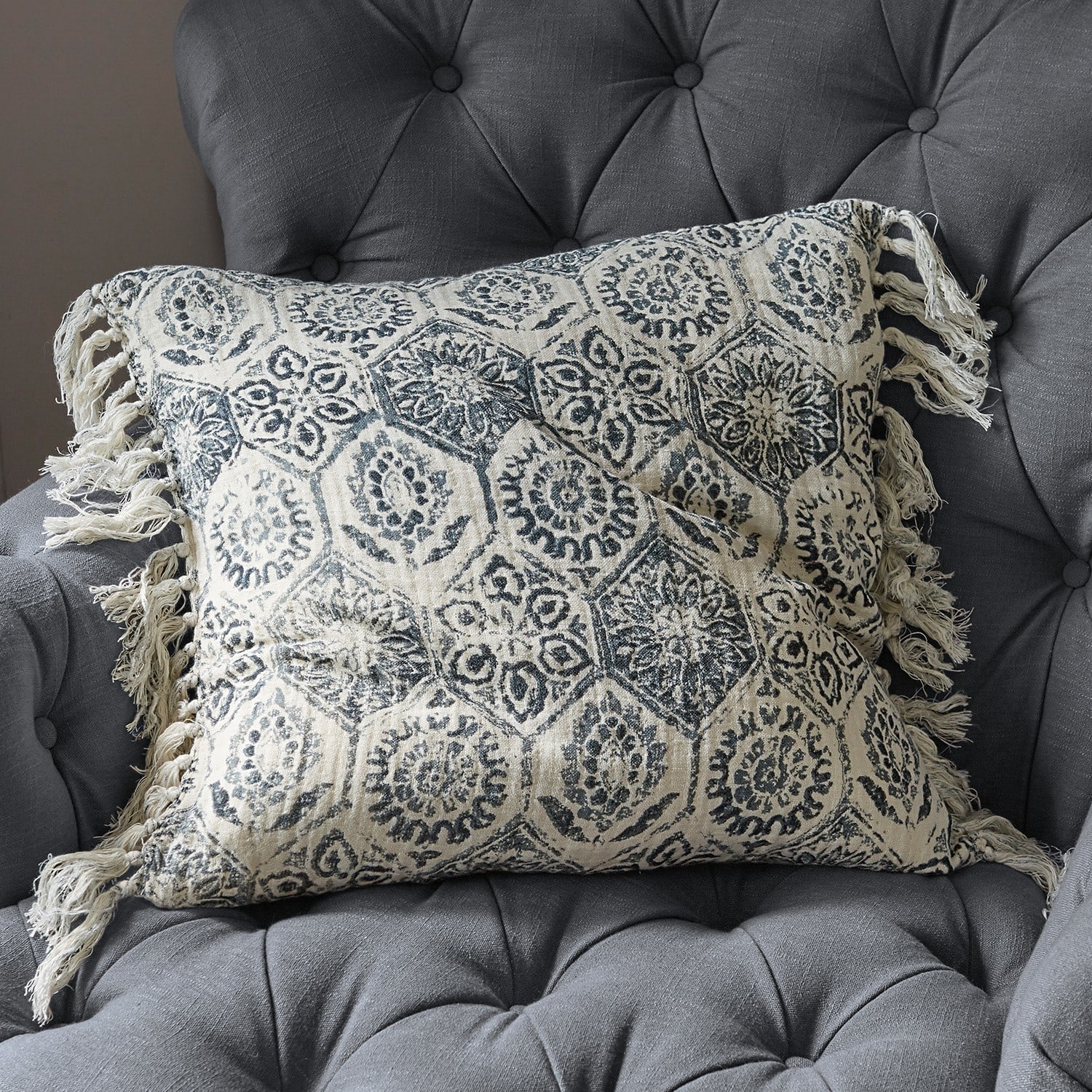 Coussin Beaupuy Coussin en coton beige avec motif bleu marine et franges sur un fauteuil gris capitonné