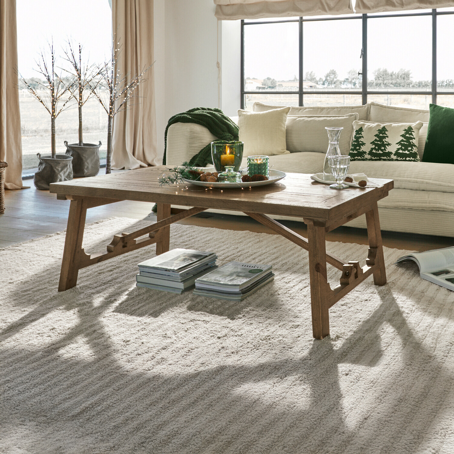 Table basse Flemming Table basse en bois naturel sur tapis clair dans un salon cosy avec décorations et coussins verts