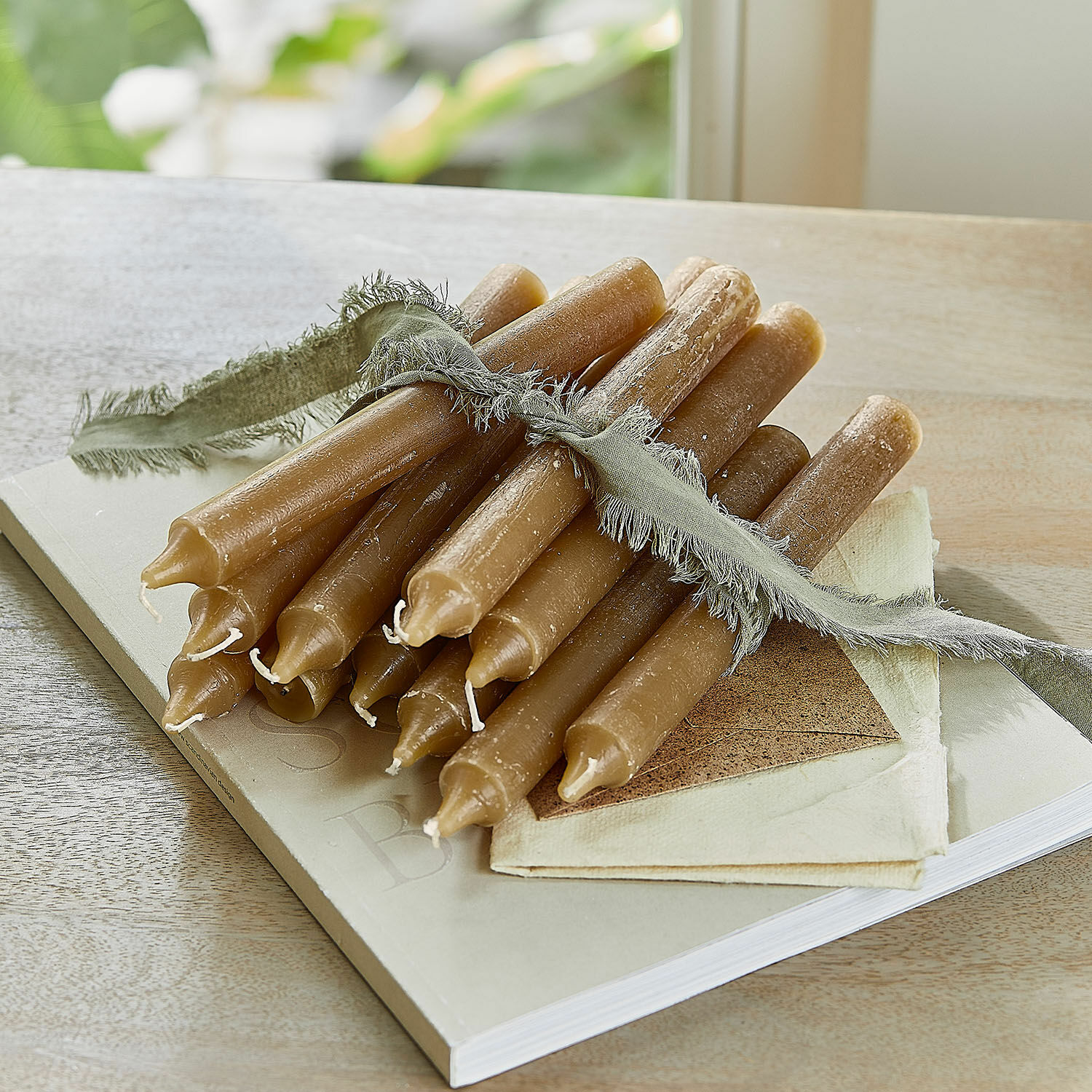 Lot de 12 bougies Bauceau Lot de bougies brunes en cire d'abeille liées par un ruban vert sur une table en bois