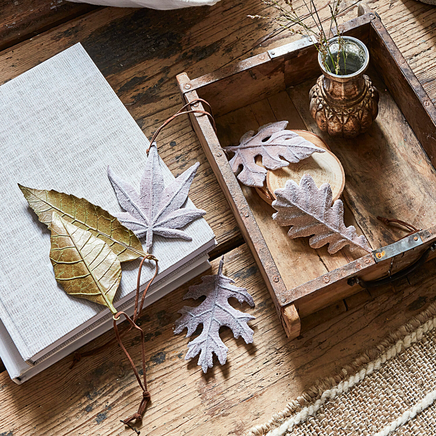 Lot de 6 feuilles décoratives Merel Feuilles décoratives dorées et grises sur une table en bois avec un livre et un plateau rustique