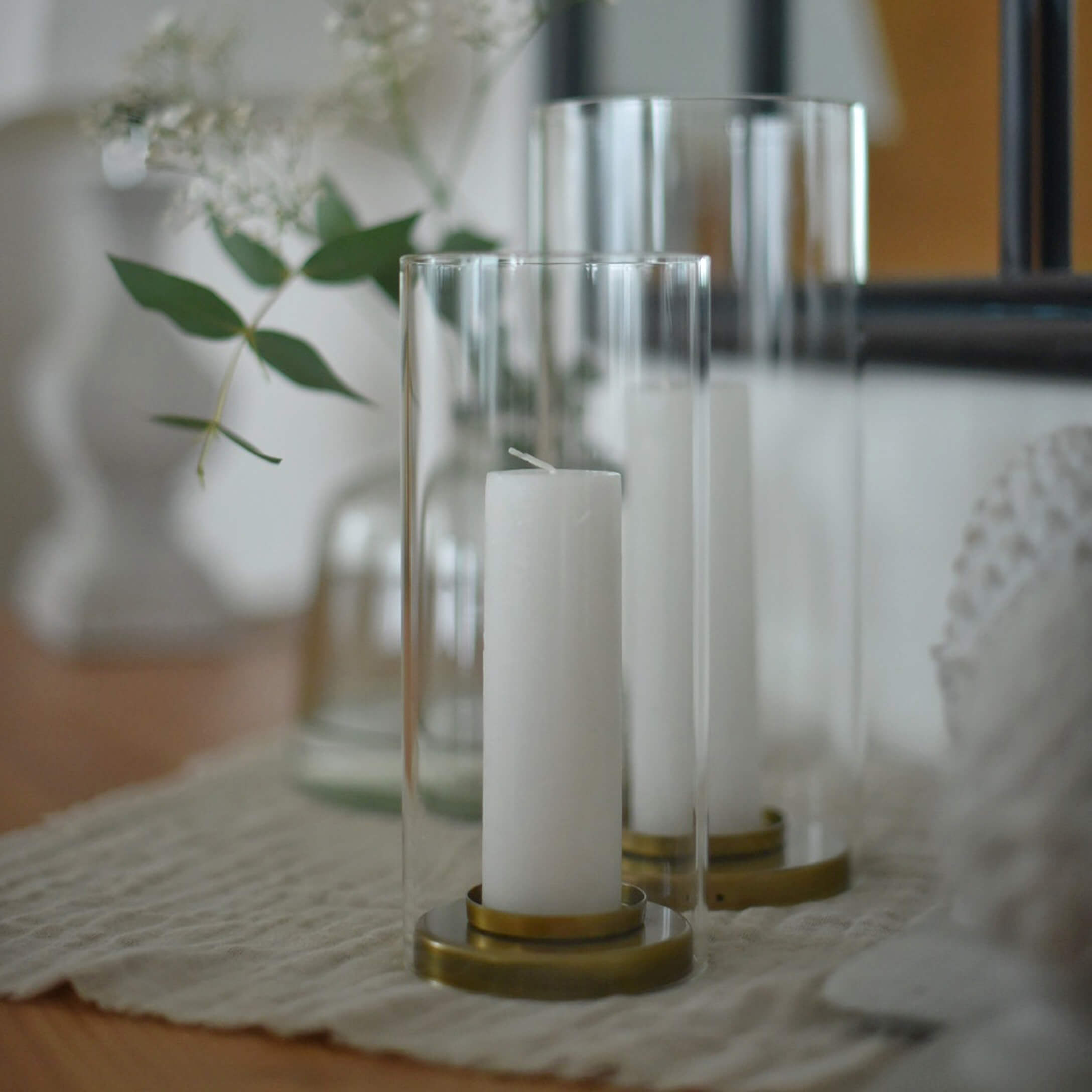 Bougies blanches dans des lanternes en verre transparent avec base en laiton sur nappe beige