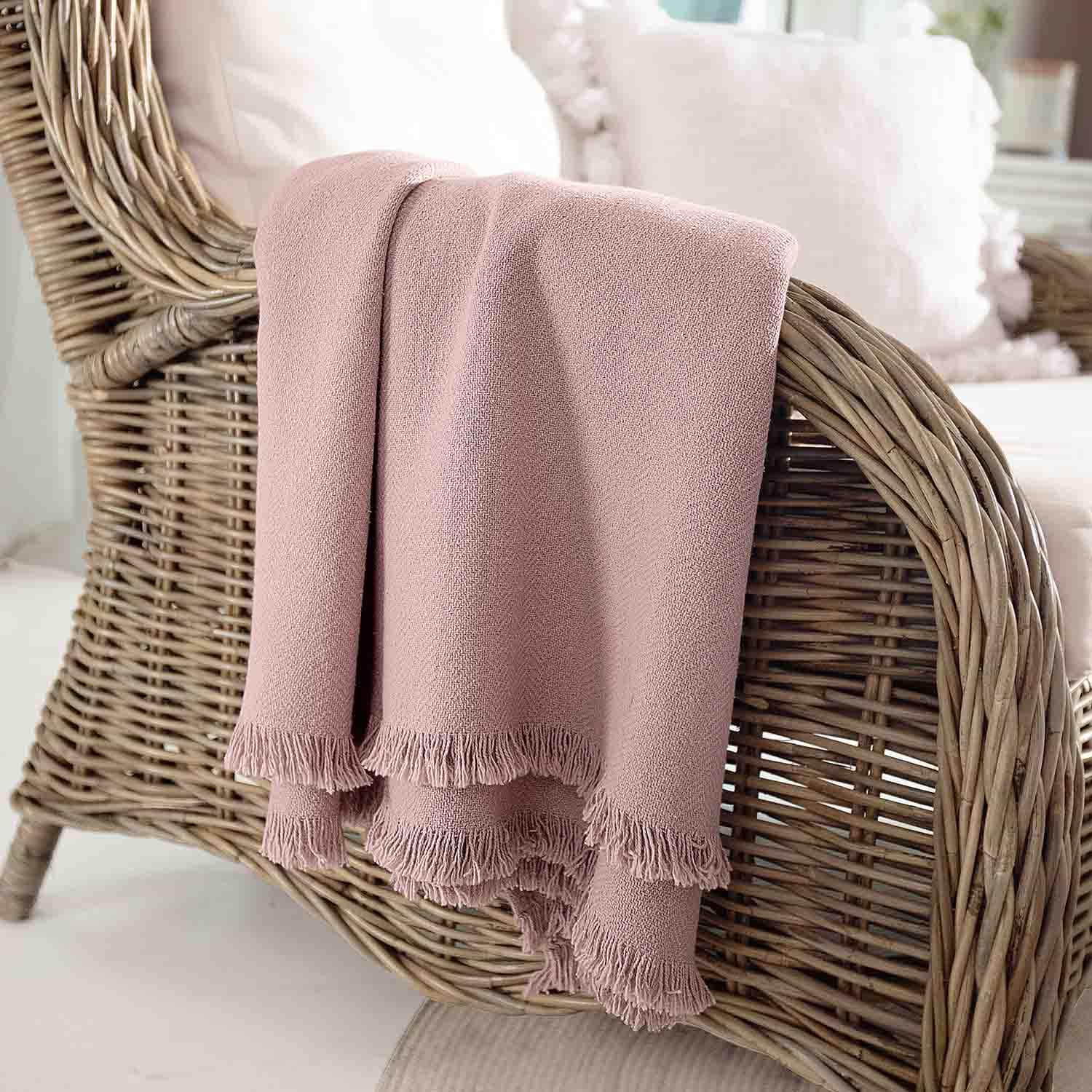 Plaid rose en tissu doux avec franges sur fauteuil en osier, décoration intérieure et confort
