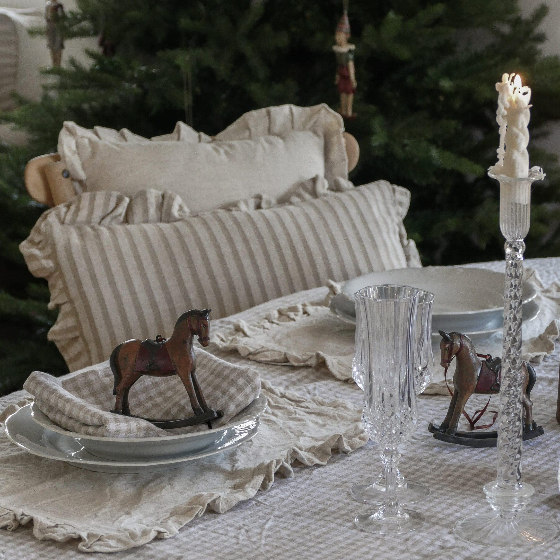 Table rustique avec nappe en lin beige à rayures, coussins assortis et décorations cheval à bascule en bois