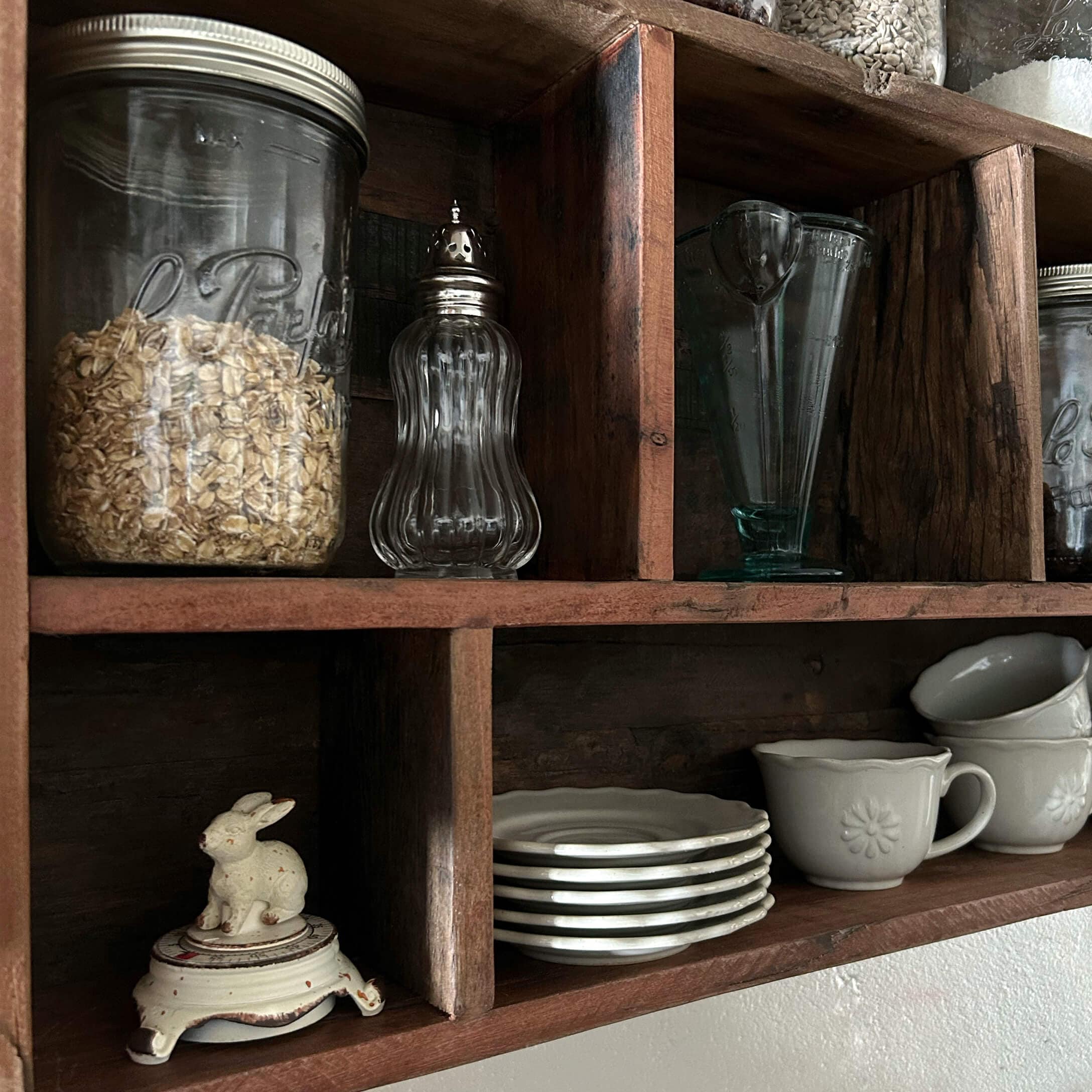 Étagère en bois avec bocaux en verre transparents et vaisselle blanche en céramique