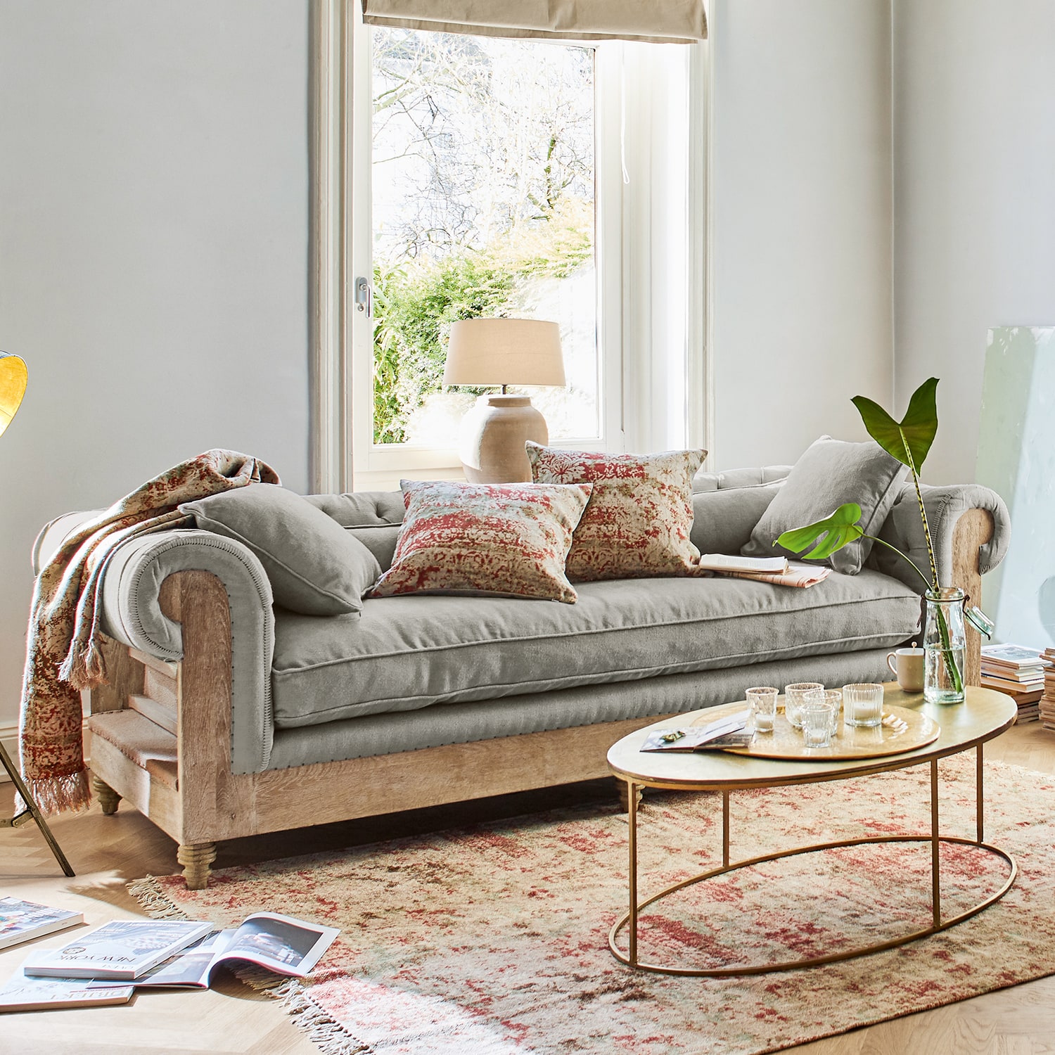 Canapé gris avec cadre en bois et coussins décoratifs dans un salon lumineux avec fenêtre