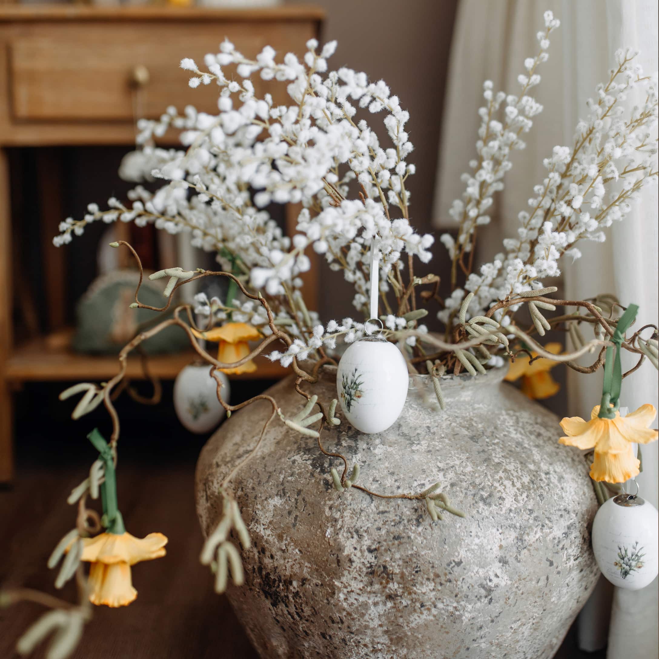 Vase en pierre grise avec branches décoratives et ornements de Pâques aux couleurs pastel