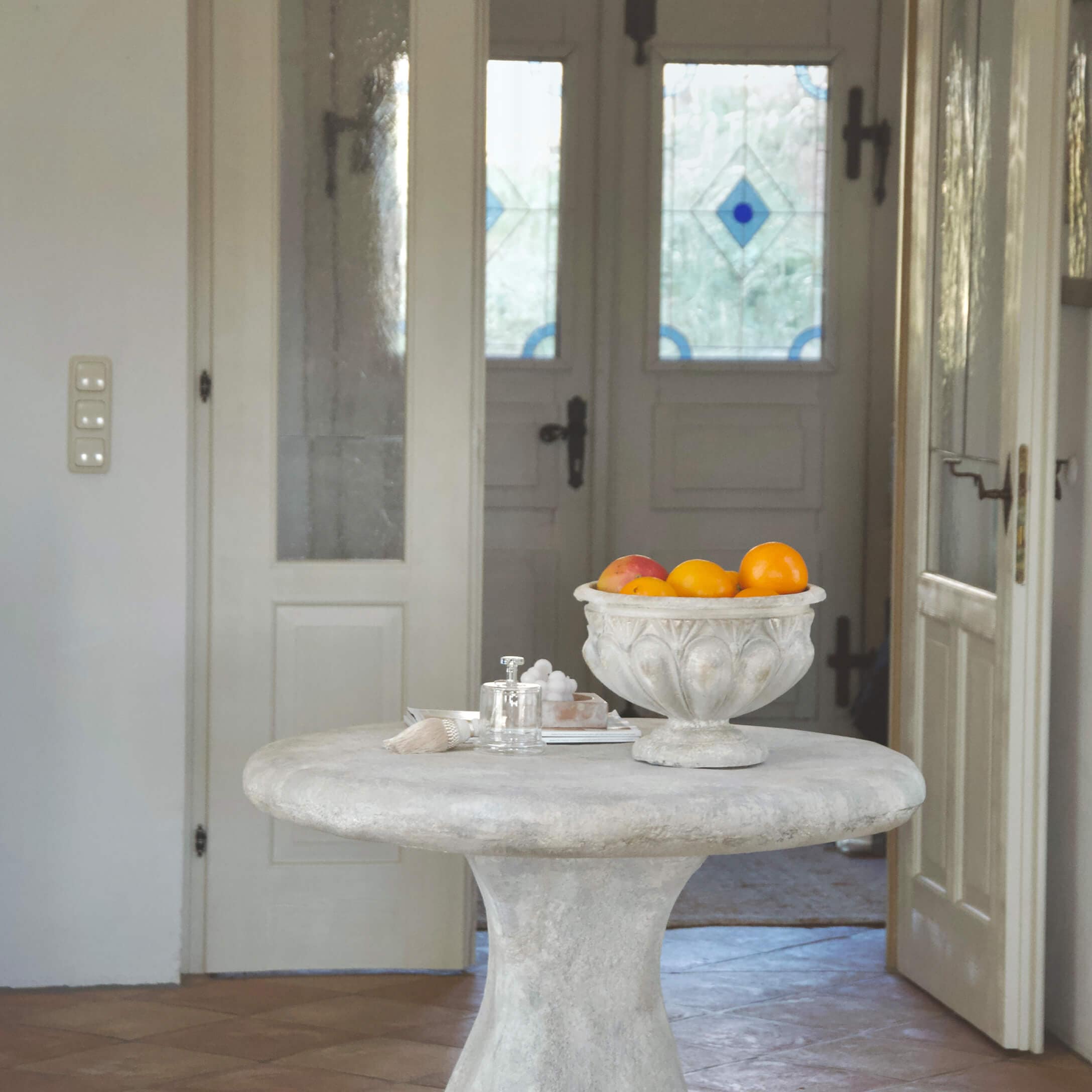 Table ronde en béton clair avec un bol décoratif vintage rempli de fruits oranges