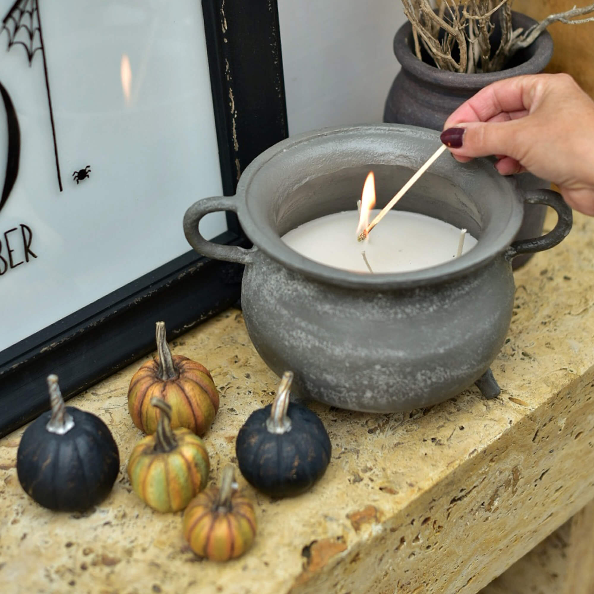 Bougie en céramique grise en forme de chaudron avec cire blanche et petites citrouilles décoratives sur un rebord en pierre
