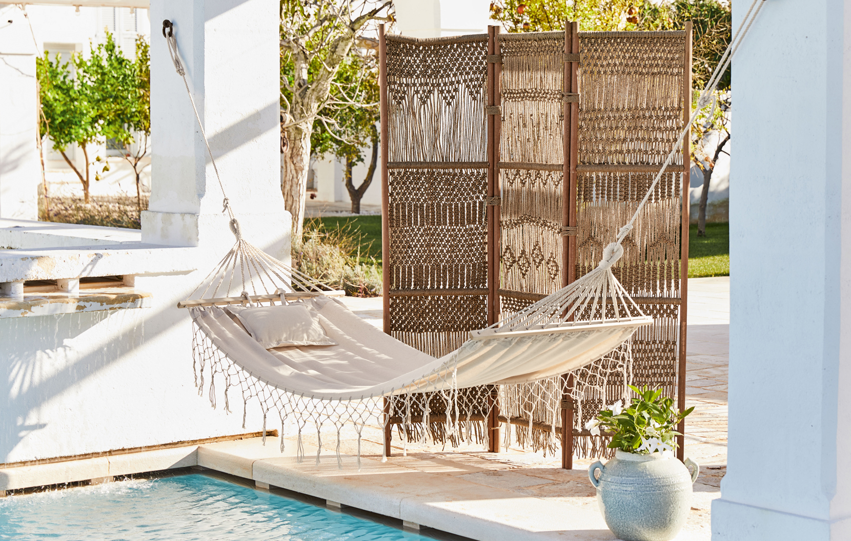 Hamac beige avec coussin et paravent tissé sur terrasse au bord de la piscine style bohème