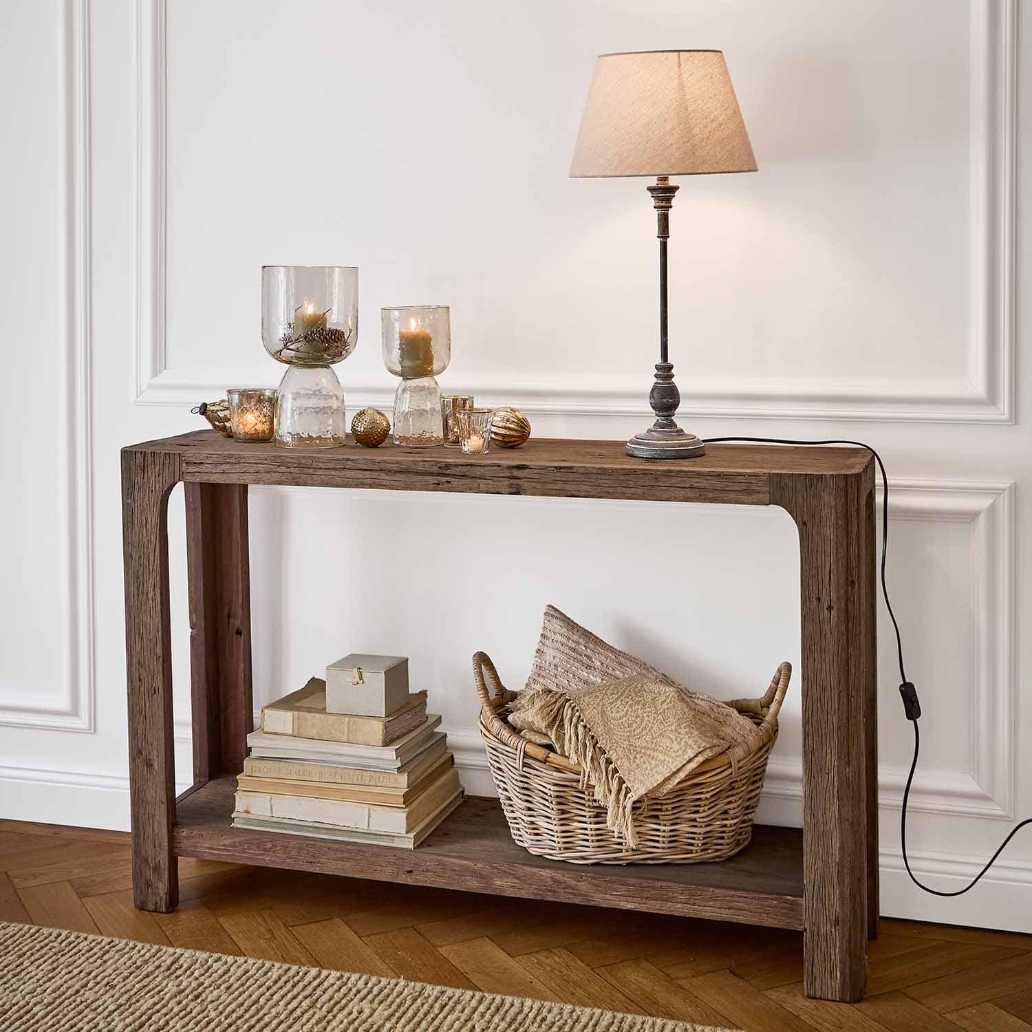 Console en bois avec lampe de table, bougies dans des photophores en verre et panier en osier avec textiles
