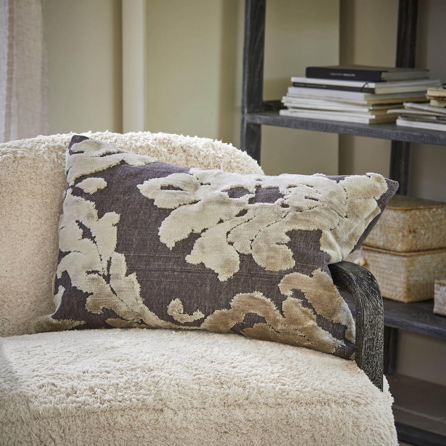 Coussin décoratif beige à motif sur fond gris foncé posé sur un fauteuil crème dans un salon