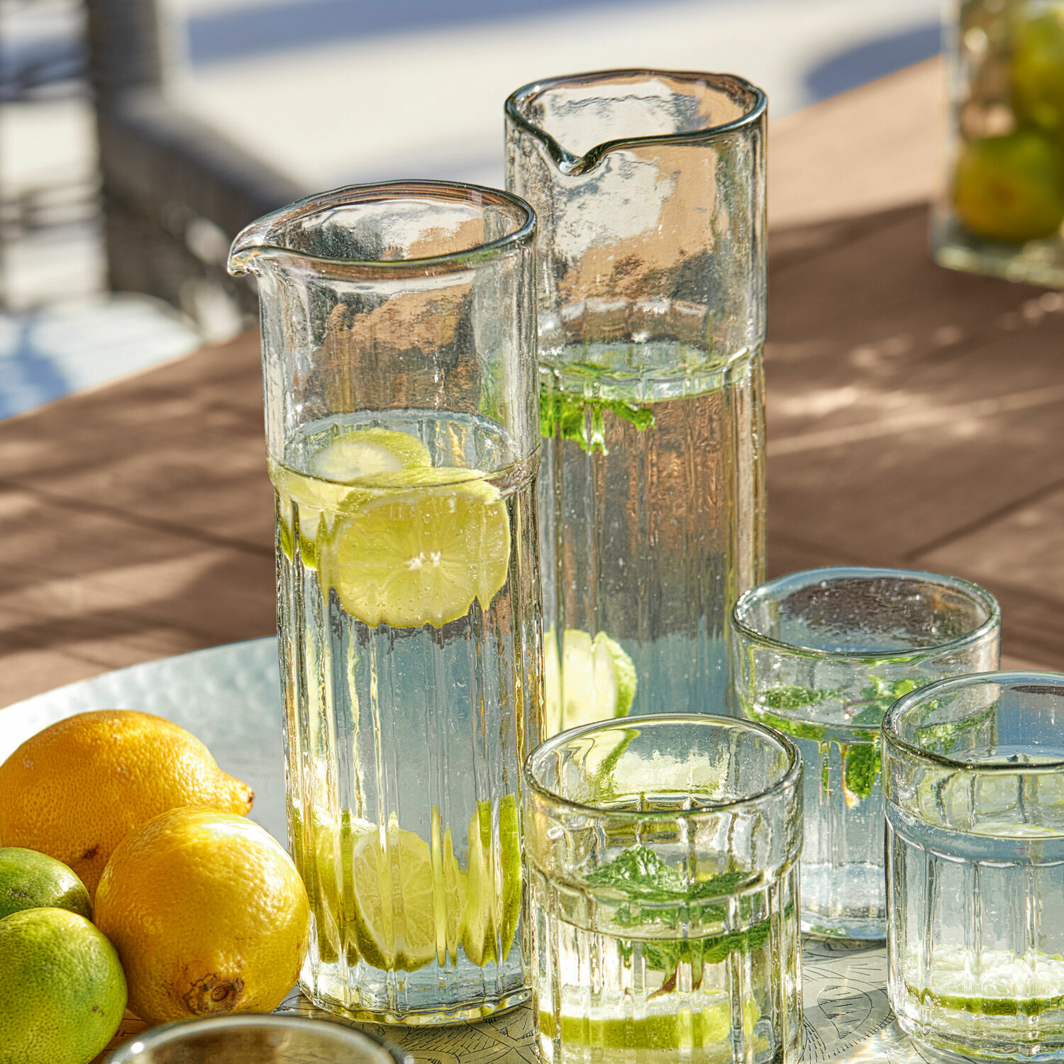 Carafes et verres en verre avec eau, citron et menthe sur table, boisson rafraîchissante d'été