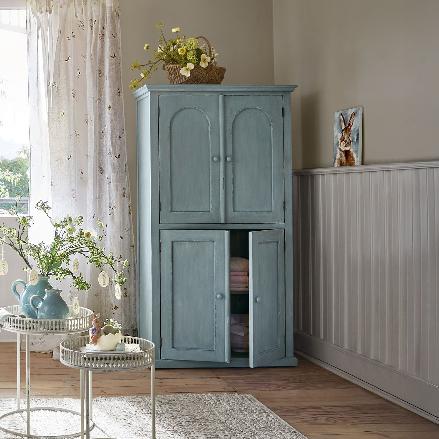 Armoire en bois bleu à deux portes dans une pièce lumineuse décorée pour le printemps avec des fleurs et des objets décoratifs