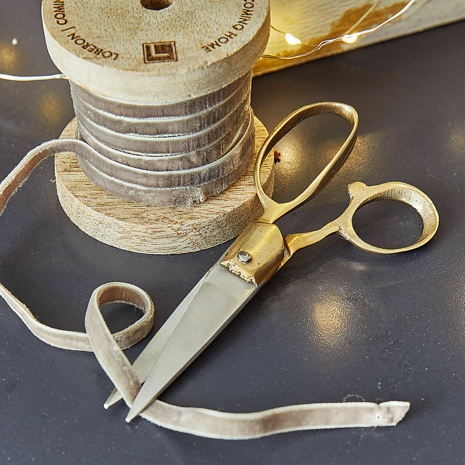 Ciseaux Sterre Ciseaux dorés et ruban en velours beige sur bobine en bois sur table sombre pour couture et décoration