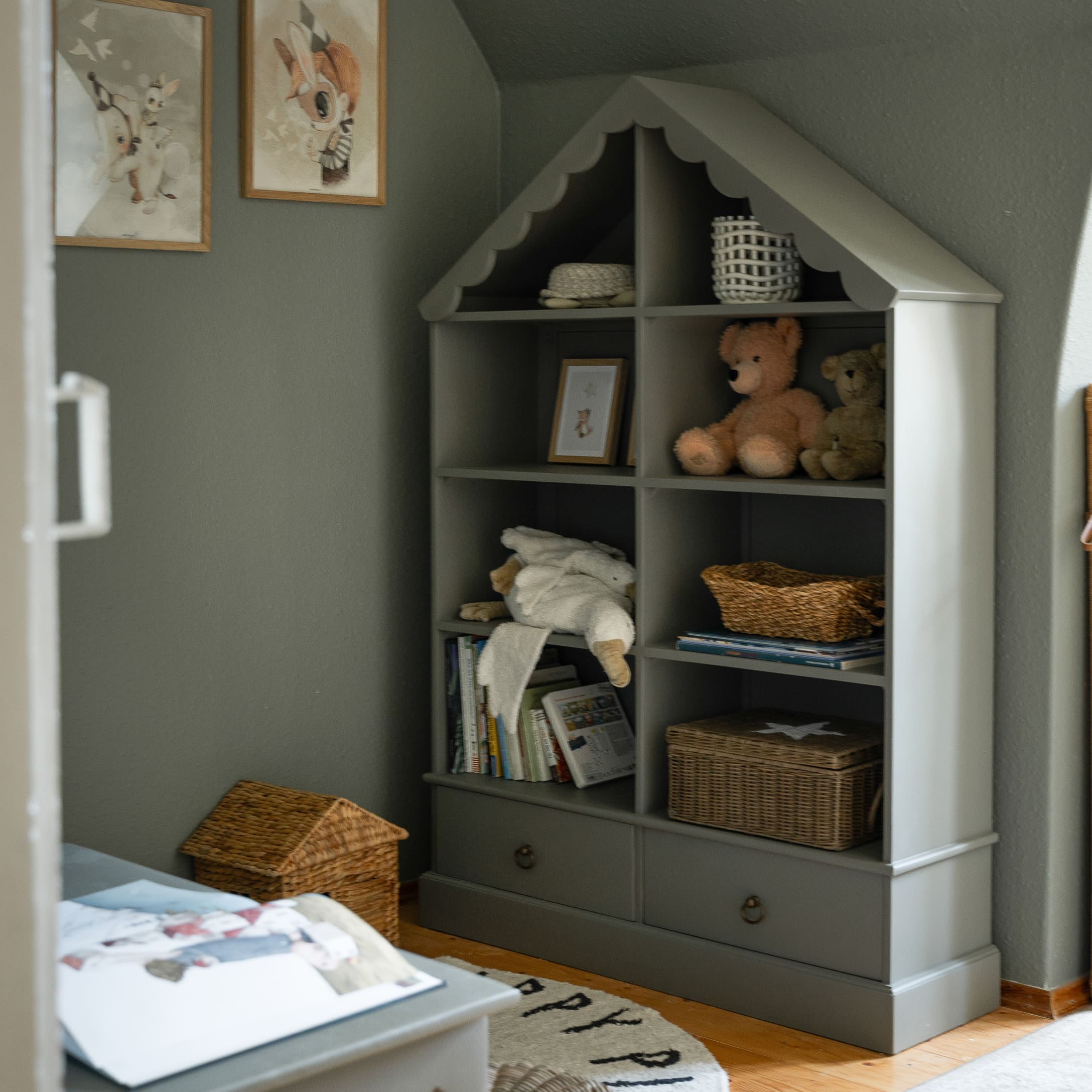 Étagère grise en bois en forme de maison avec peluches et paniers dans une chambre d'enfant