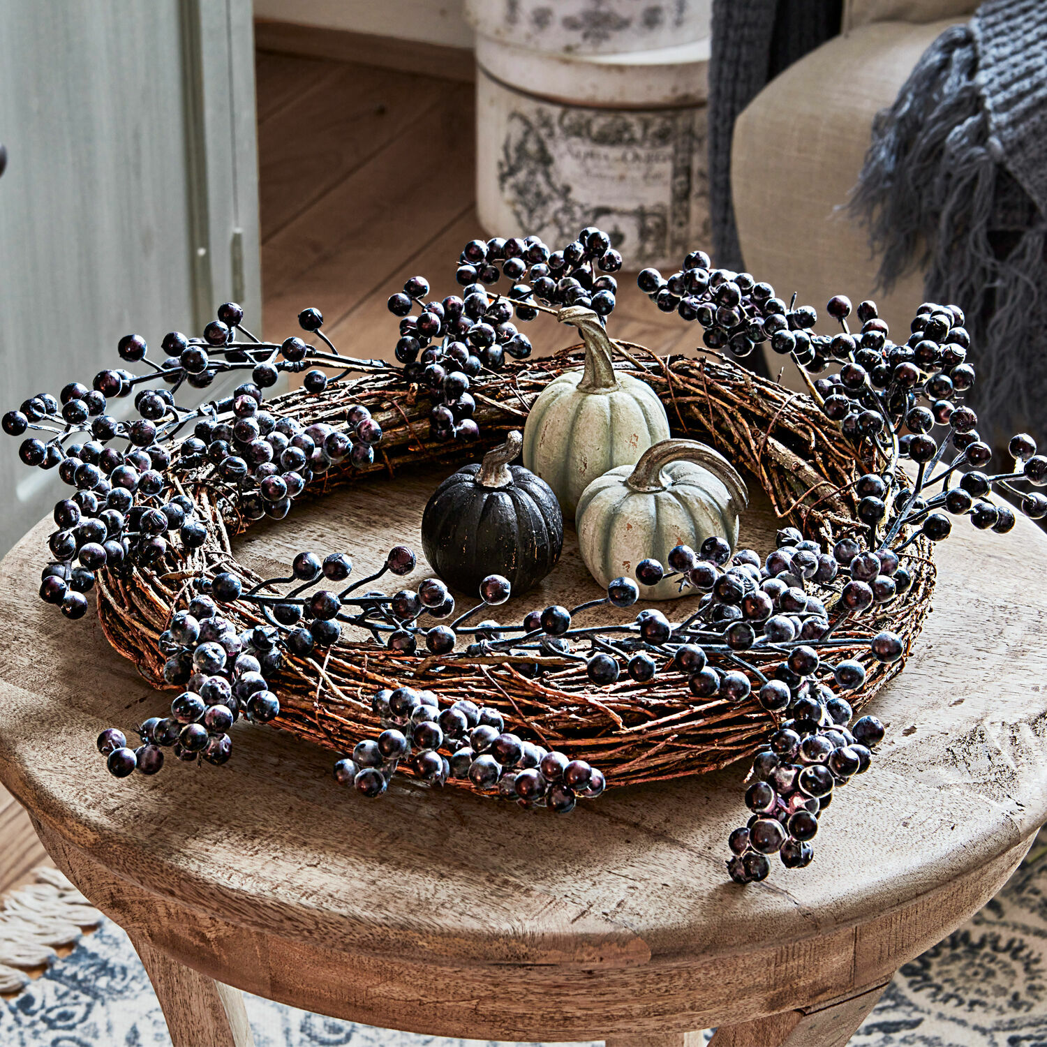 Couronne Isabeau Couronne décorative en branches avec baies noires et petites citrouilles sur table en bois