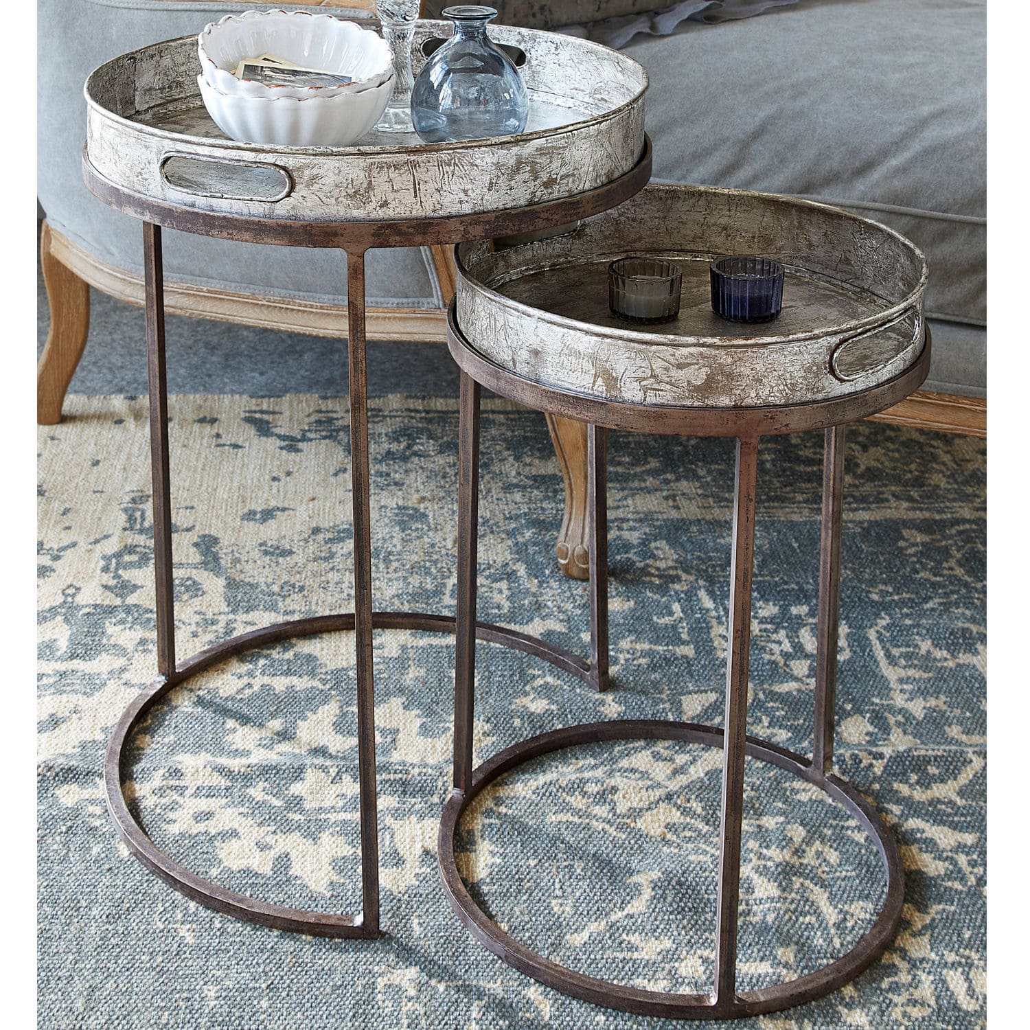 Lot de 2 tables d’appoint Saint Mark Ensemble de deux tables rondes avec cadres métalliques et plateaux argentés sur tapis dans un salon