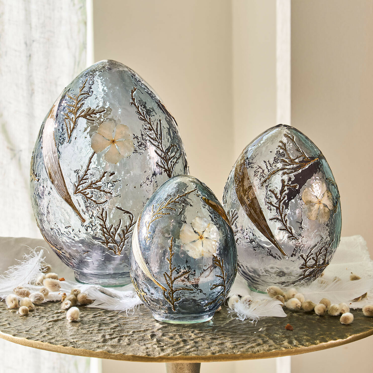 Lot de 3 œufs décoratifs Lunavelle Ensemble de trois œufs décoratifs en verre gris avec fleurs et feuilles incrustées posés sur une table
