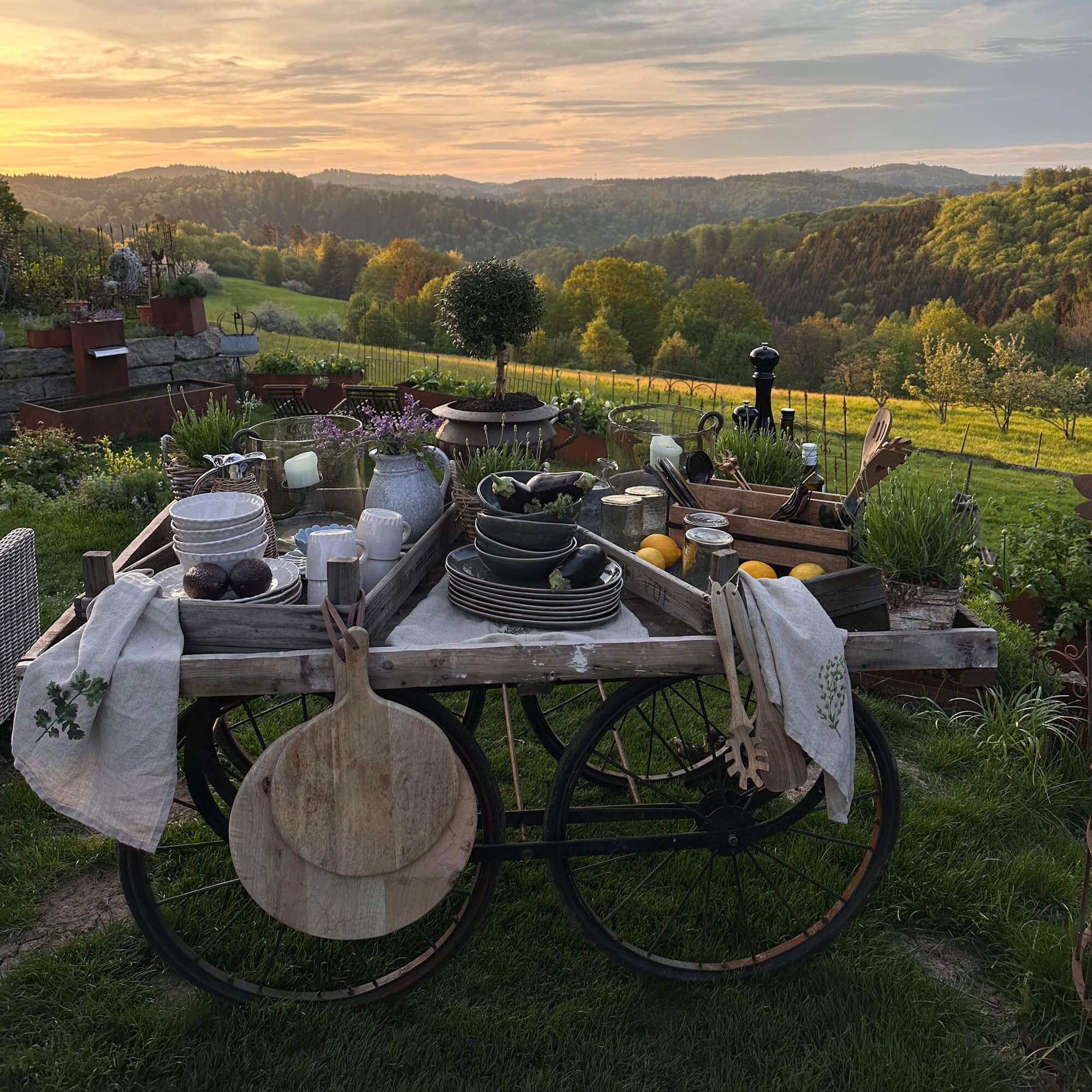 Chariot en bois rustique avec vaisselle et décorations dans un jardin verdoyant au coucher du soleil
