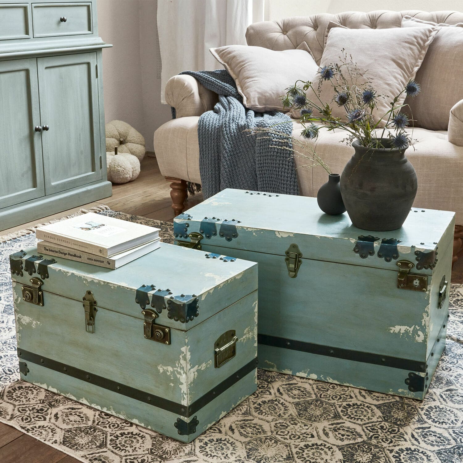 Lot de 2 malles Gorman Deux coffres en bois bleu avec ferrures métalliques sur un tapis dans un salon avec canapé beige