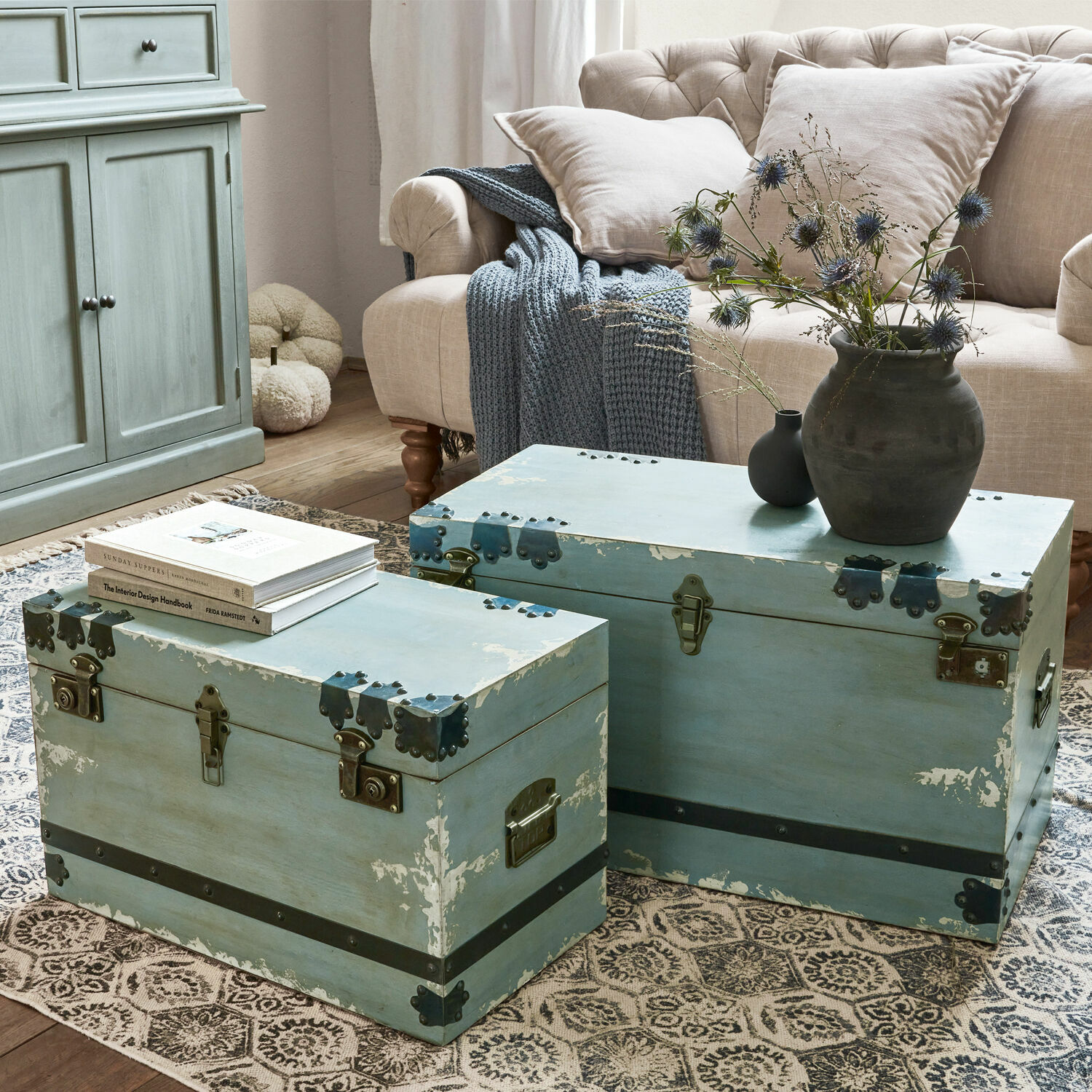 Lot de 2 malles Gorman Deux coffres en bois bleu avec ferrures métalliques sur un tapis dans un salon avec canapé beige