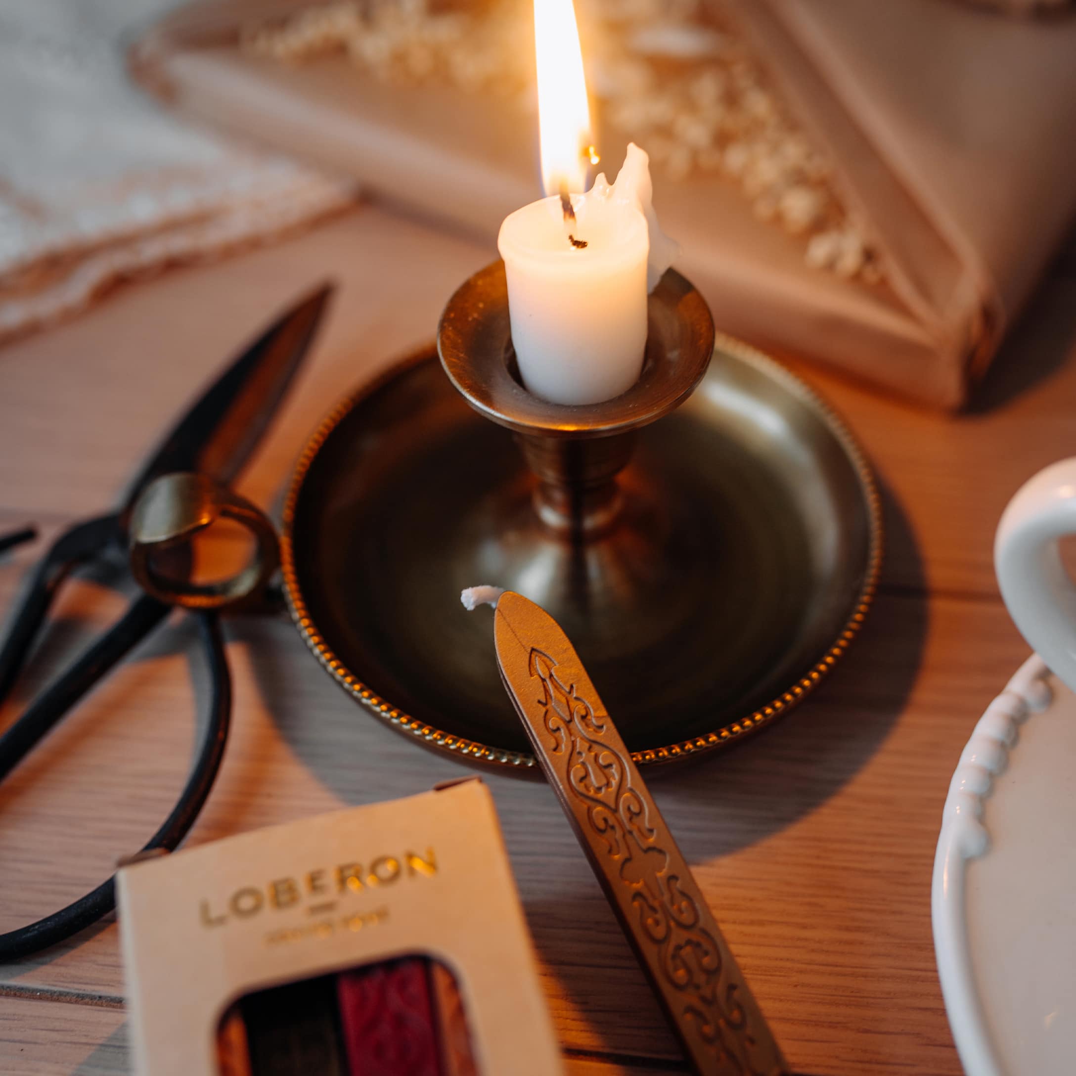 Bougie blanche allumée dans un chandelier en laiton sur une table en bois avec outils d'emballage