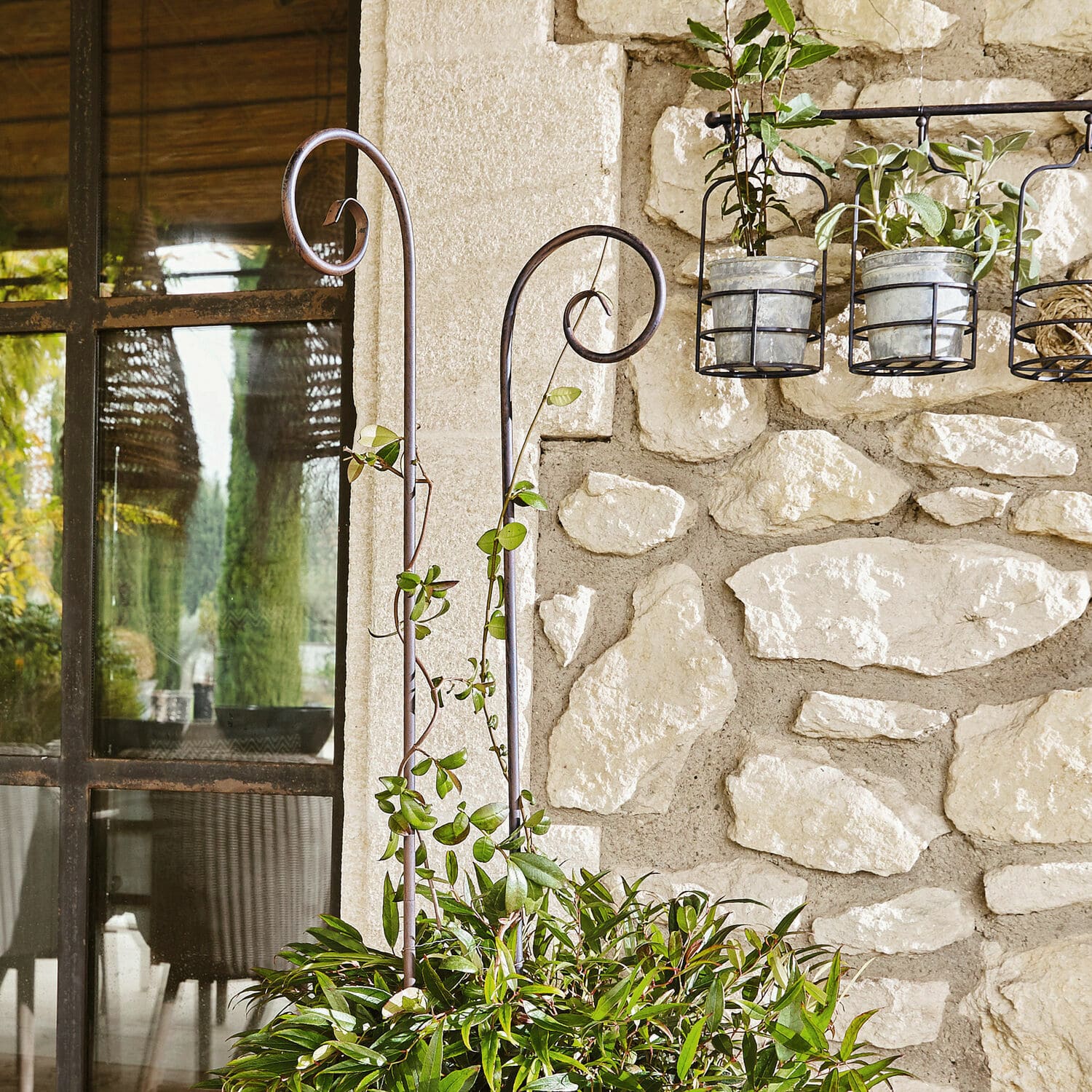 Supports métalliques décoratifs pour plantes dans un jardin avec mur en pierre et feuillage vert