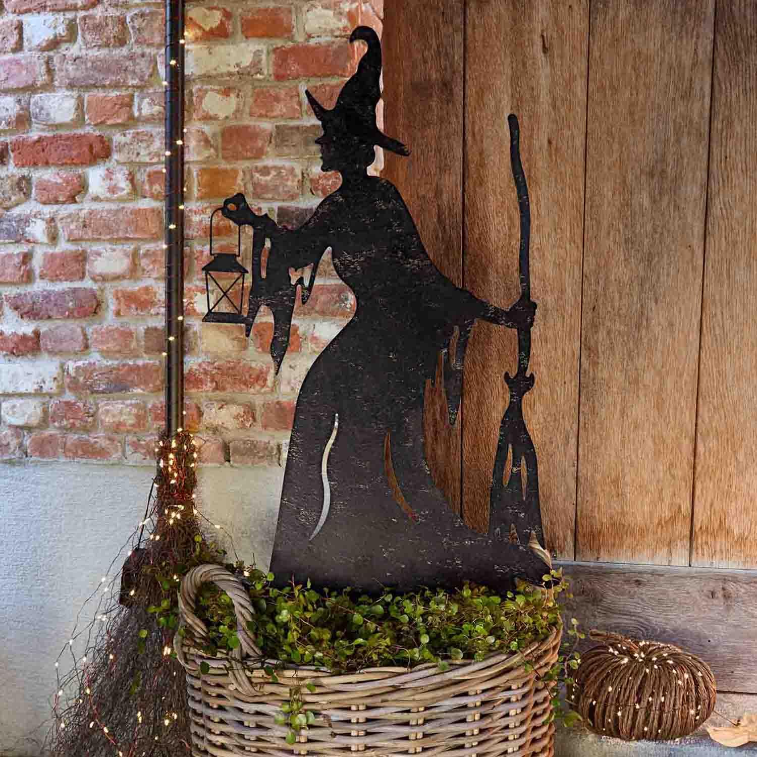 Décoration en métal silhouette de sorcière avec lanterne et balai dans un panier en osier avec verdure