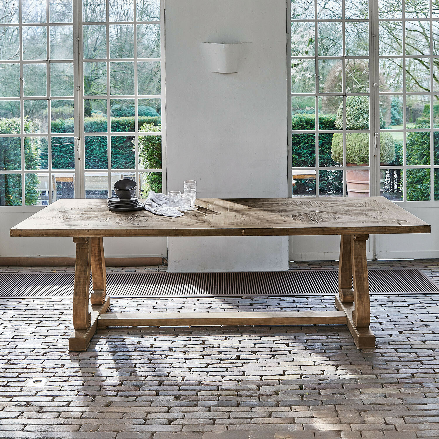 Table Campbelltown Grande table à manger en bois naturel avec plateau décoratif devant de grandes fenêtres et un sol en briques