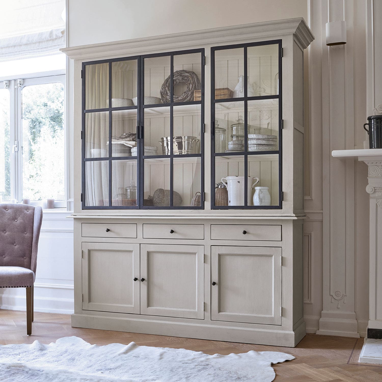 Buffet Thilot Grande vitrine en bois beige avec portes vitrées et tiroirs pour rangement dans un salon lumineux