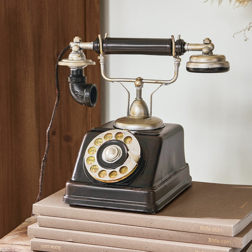 Ancien téléphone noir à cadran rotatif avec éléments métalliques posé sur une pile de livres, décoration vintage