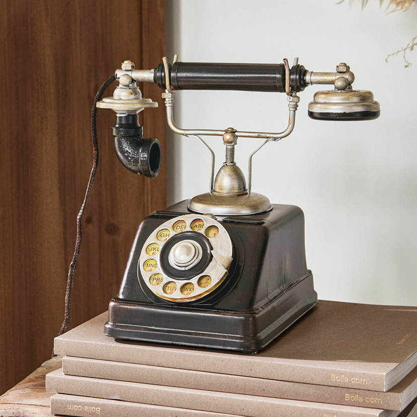 Ancien téléphone noir à cadran rotatif avec éléments métalliques posé sur une pile de livres, décoration vintage