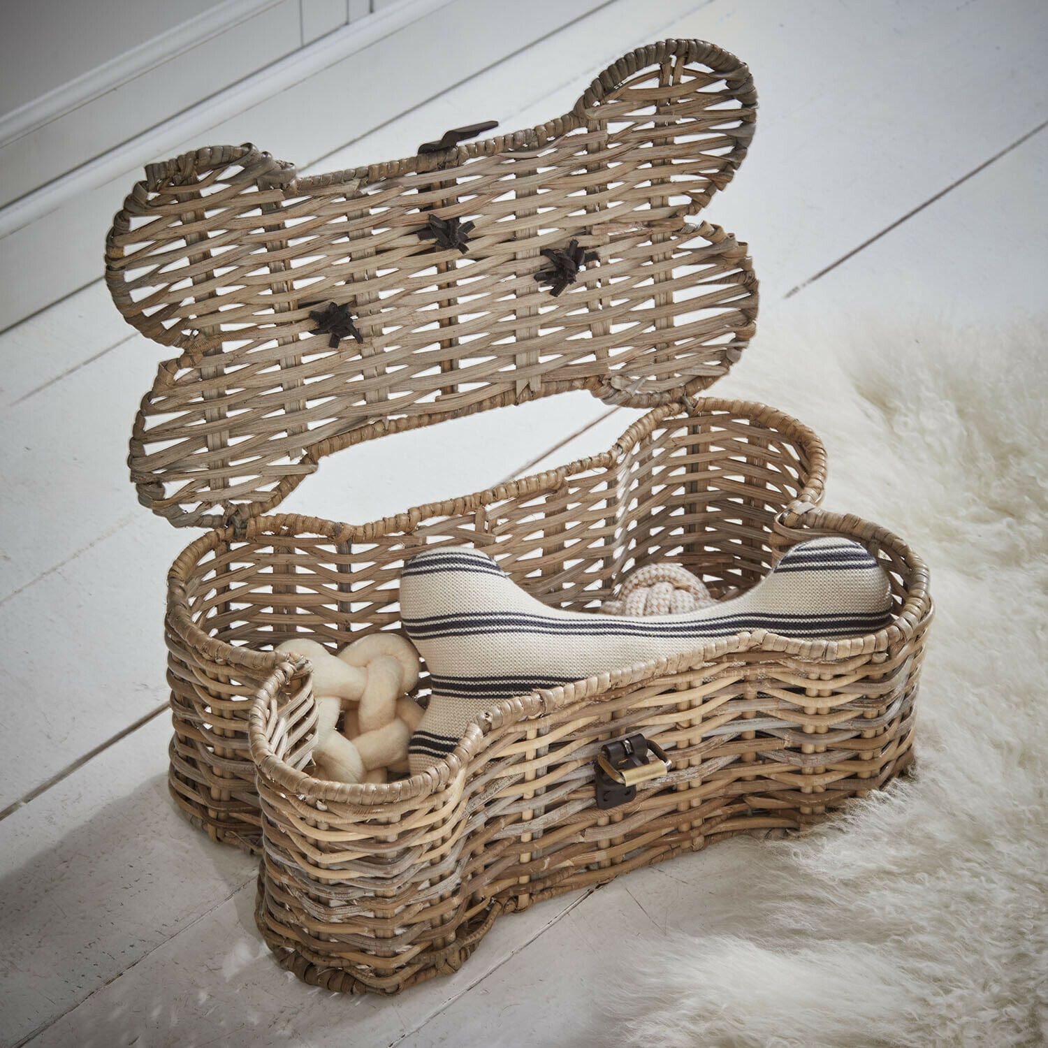 Malle pour animaux Nuzzlea Panier en rotin en forme d'os avec jouets pour chien en couleur naturelle sur un sol blanc