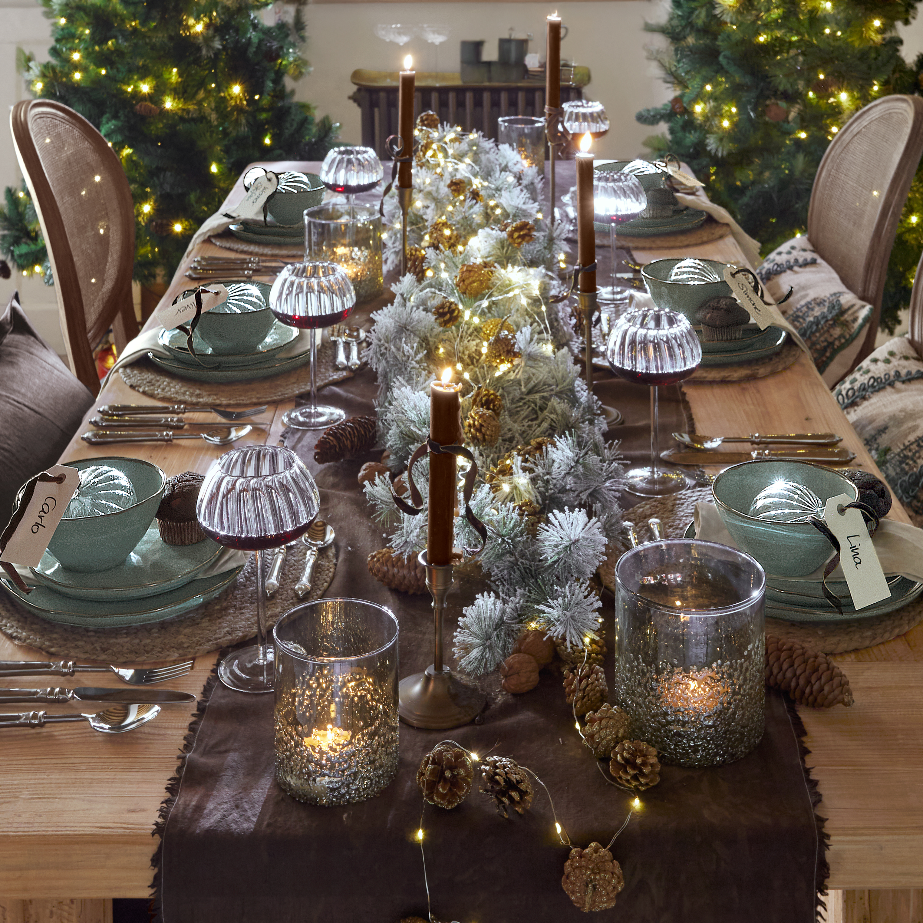 Table de Noël décorée avec vaisselle en céramique verte, bougies et guirlandes lumineuses sur bois naturel