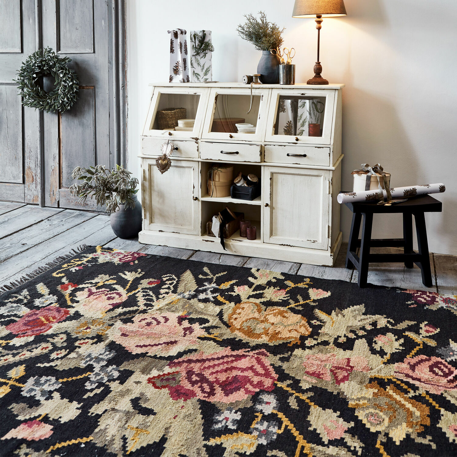 Tapis Matteo Tapis à motif floral foncé devant un buffet en bois blanc vieilli sur un sol en bois gris