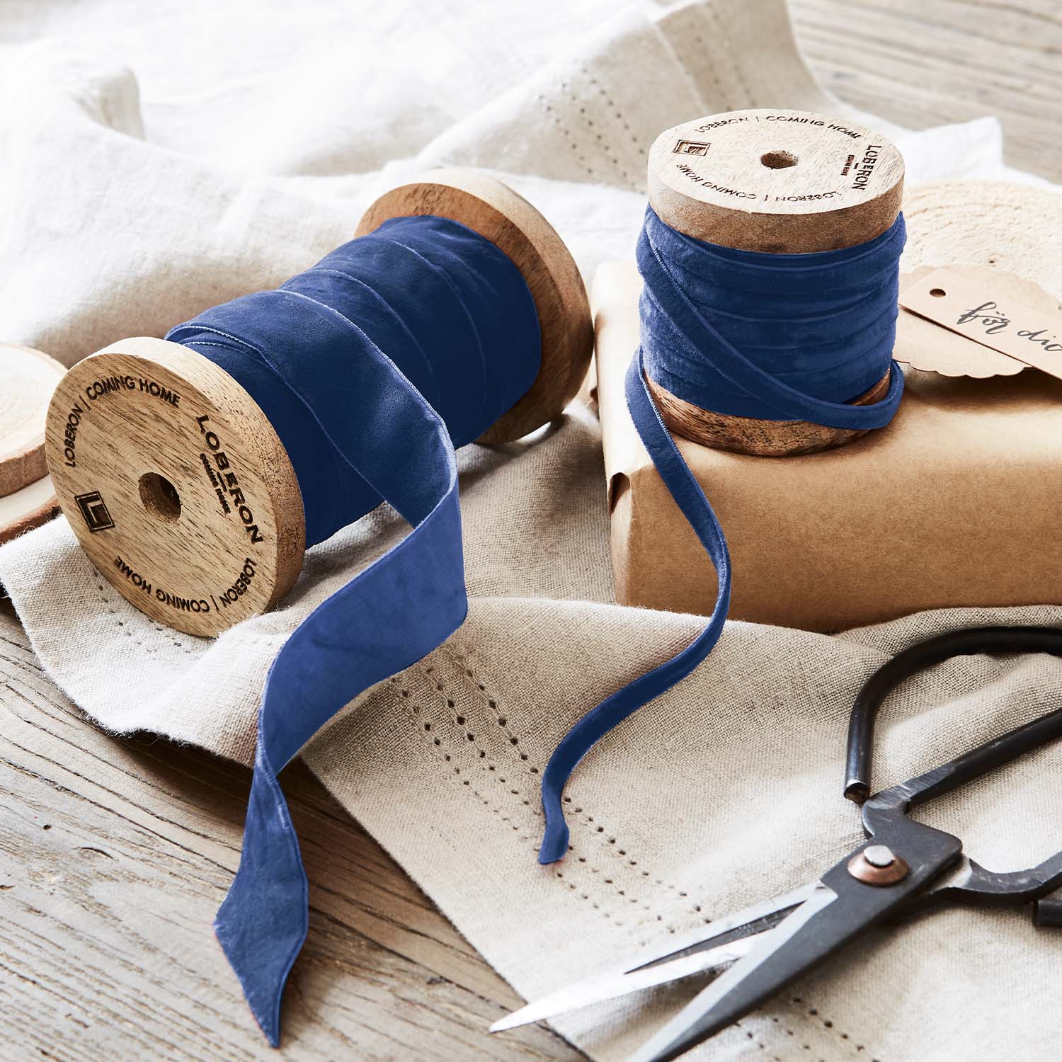 Ruban en velours bleu enroulé sur bobines en bois avec ciseaux sur tissu en lin pour décoration et artisanat