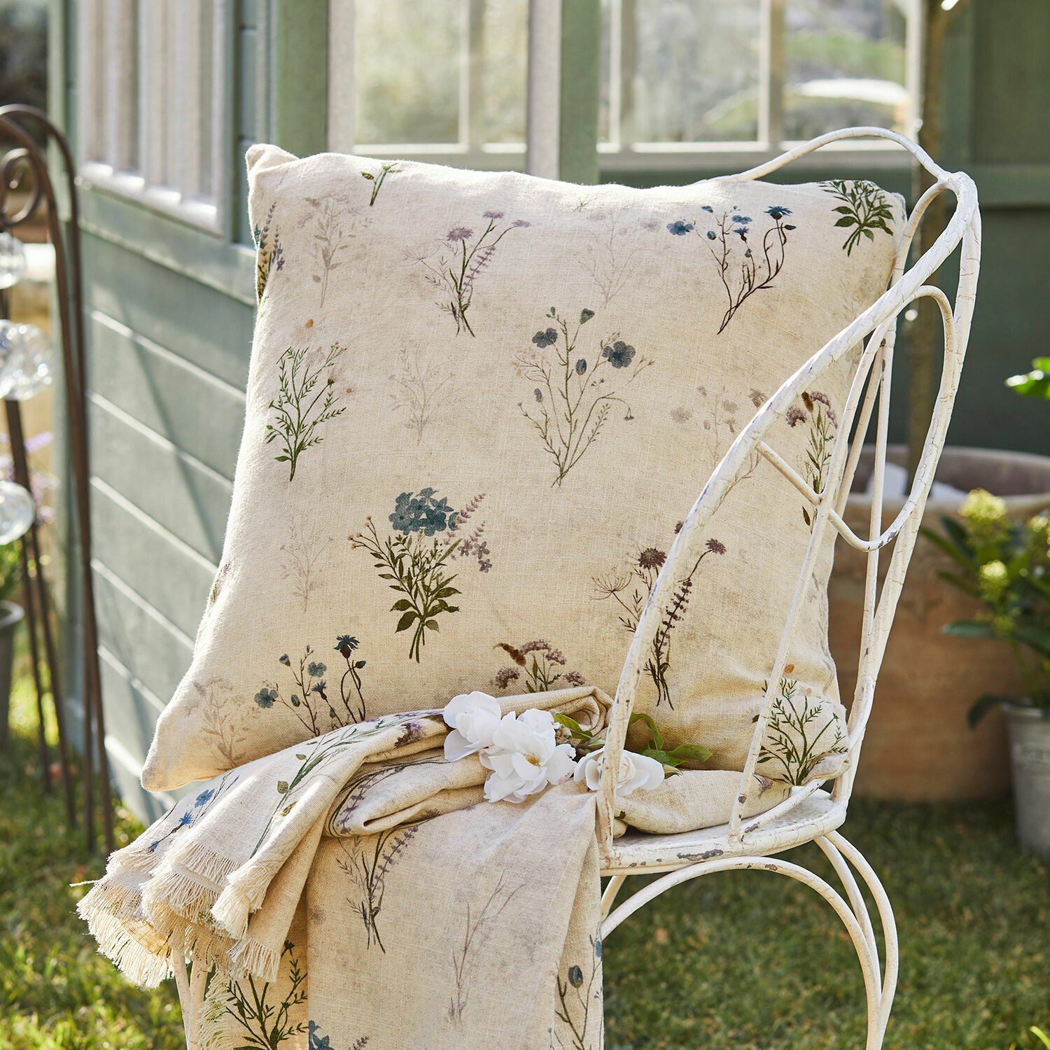 Housse de coussin Cabinda Coussin et plaid en lin beige avec motif floral délicat sur chaise en métal dans un jardin