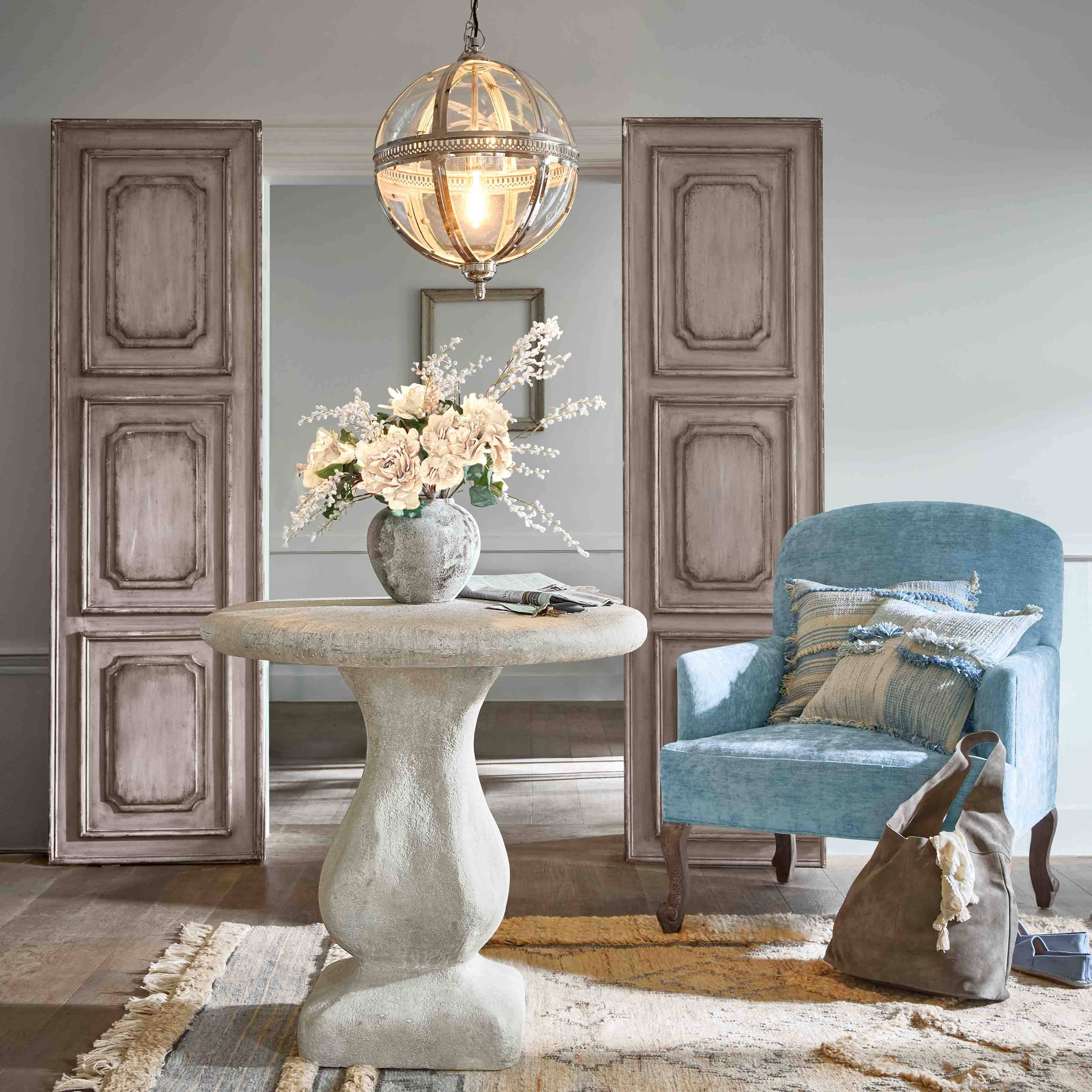 Table ronde en béton avec vase de fleurs et fauteuil bleu avec coussins dans un salon élégant