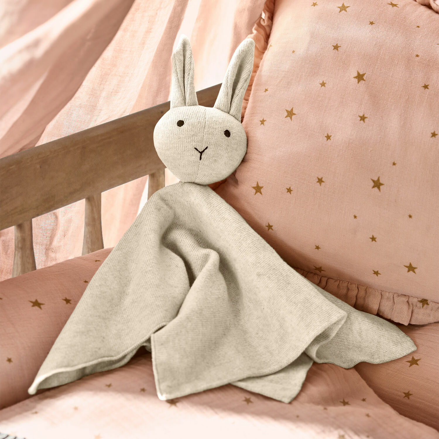 Doudou Lumiou Doudou lapin gris en tissu doux sur literie rose à étoiles, accessoire déco pour chambre d'enfant