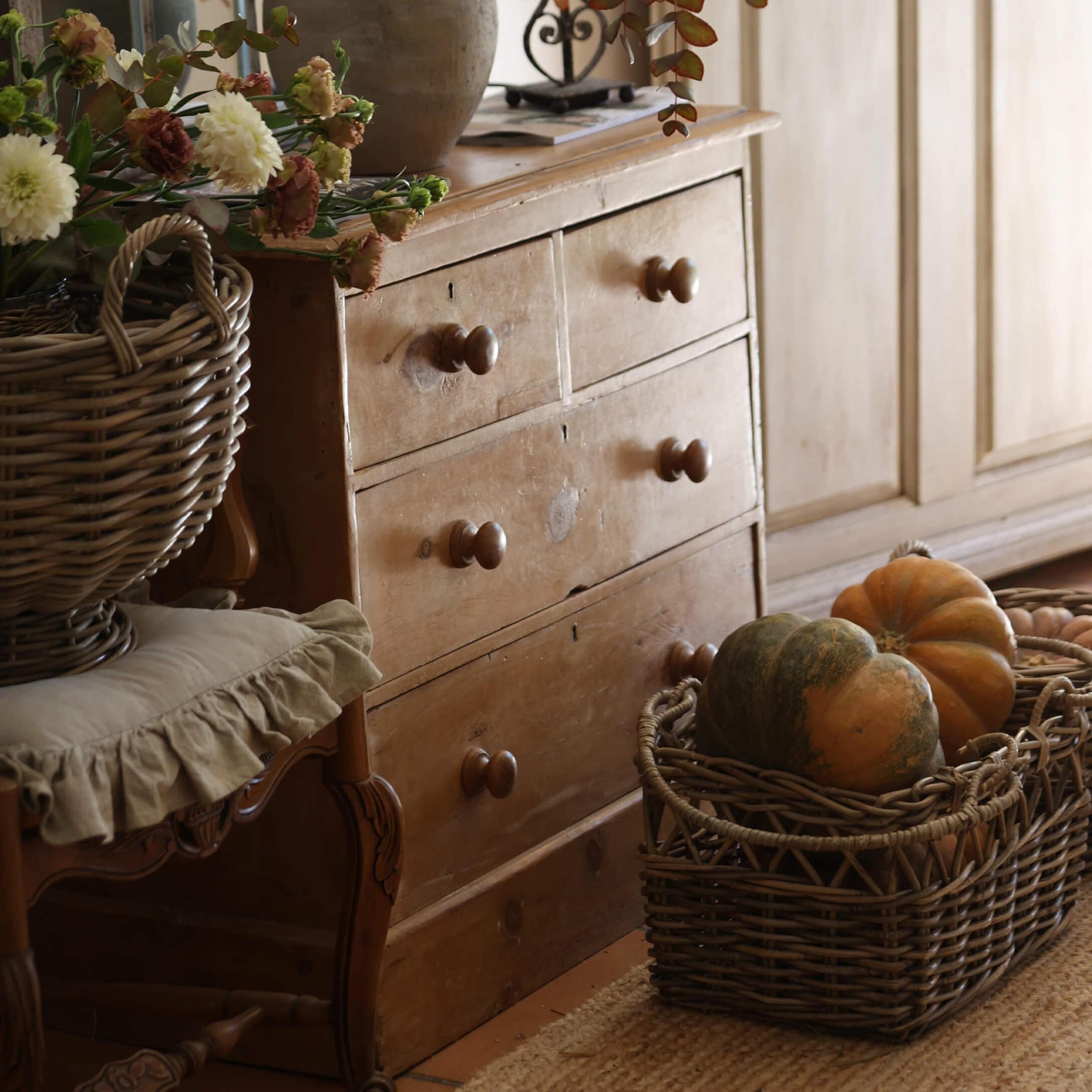 Commode rustique en bois avec quatre tiroirs et panier en osier rempli de citrouilles dans un intérieur chaleureux