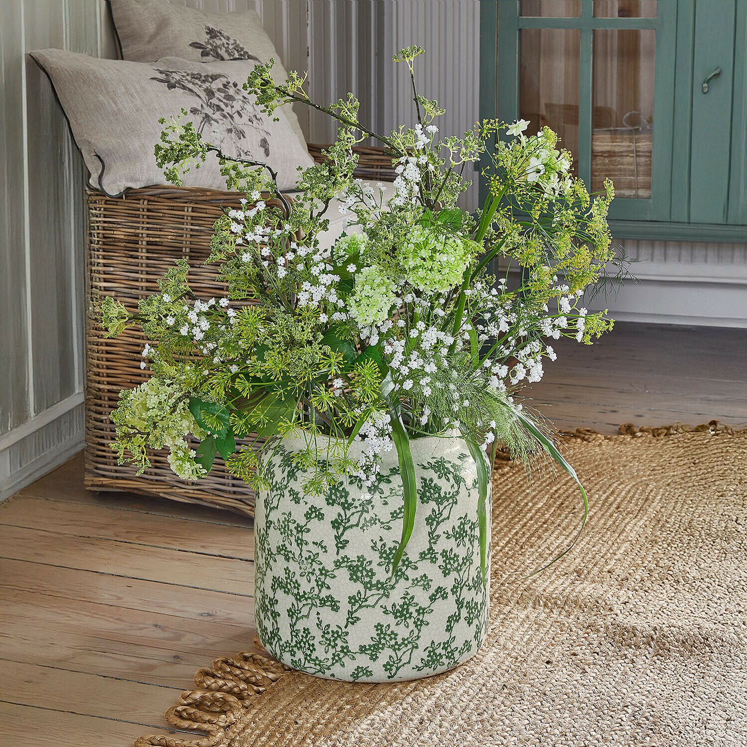 Vase Vaudrisse Vase en céramique blanche à motif vert avec fleurs blanches et feuillage vert sur parquet en bois